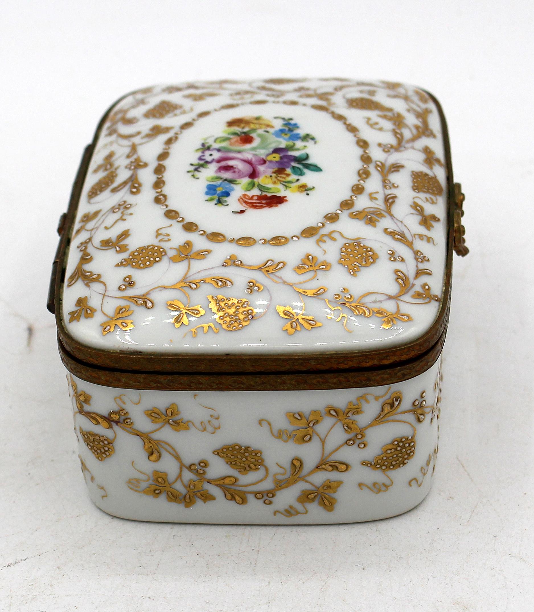 Mid-20th century porcelain trinket box by Le Tallec, Paris. Rectangular with brass fittings, the whole elegantly hand gilded with raised grapes & leaves on trailing vines, an oval floral polychromed reserve centered on the cover. Interior also with