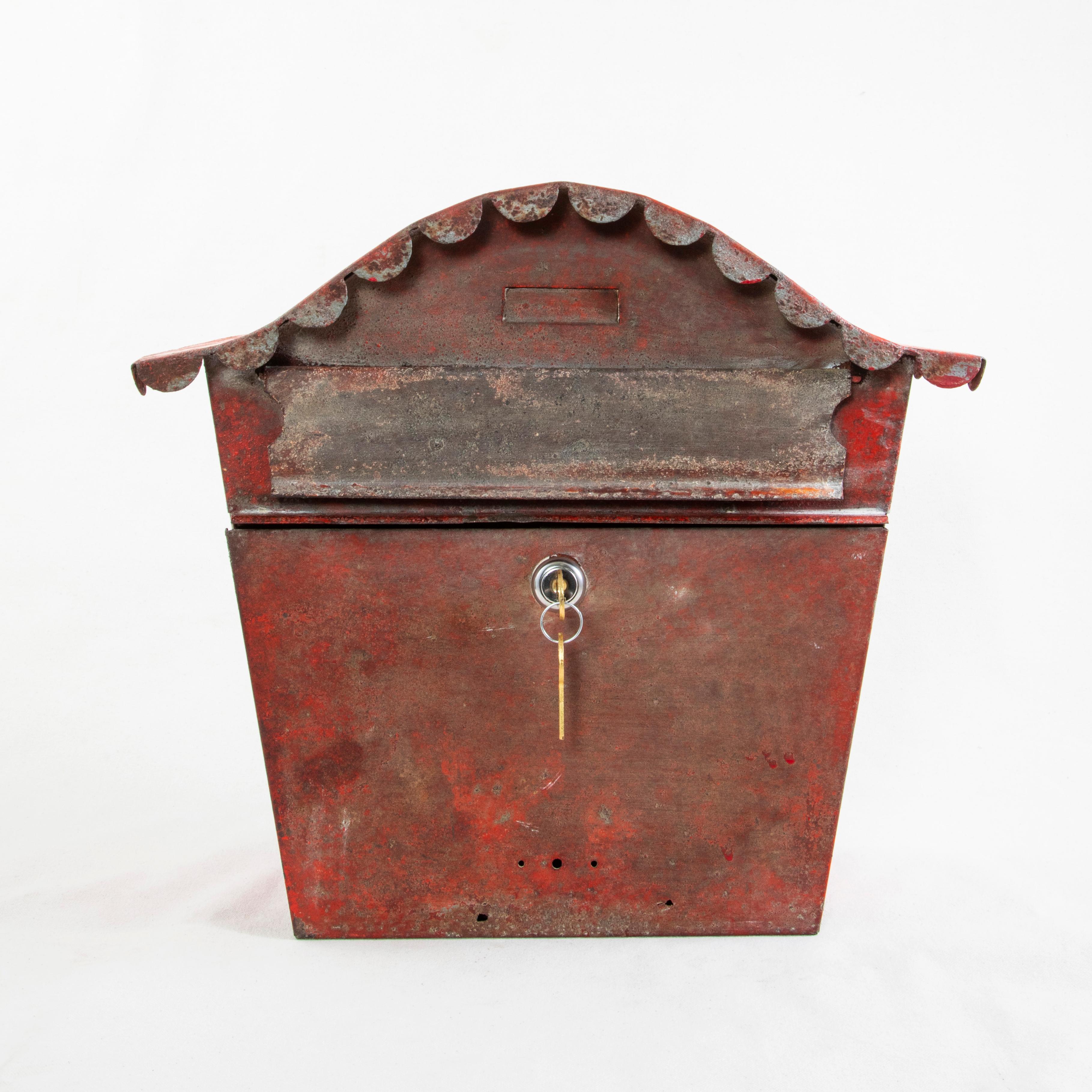 This midcentury French red painted metal mailbox features a curved top with a scalloped apron. Below the curved top is a mail slot with hinged cover and an inset rectangle above where a name or address label may be inserted. Under the slot is a