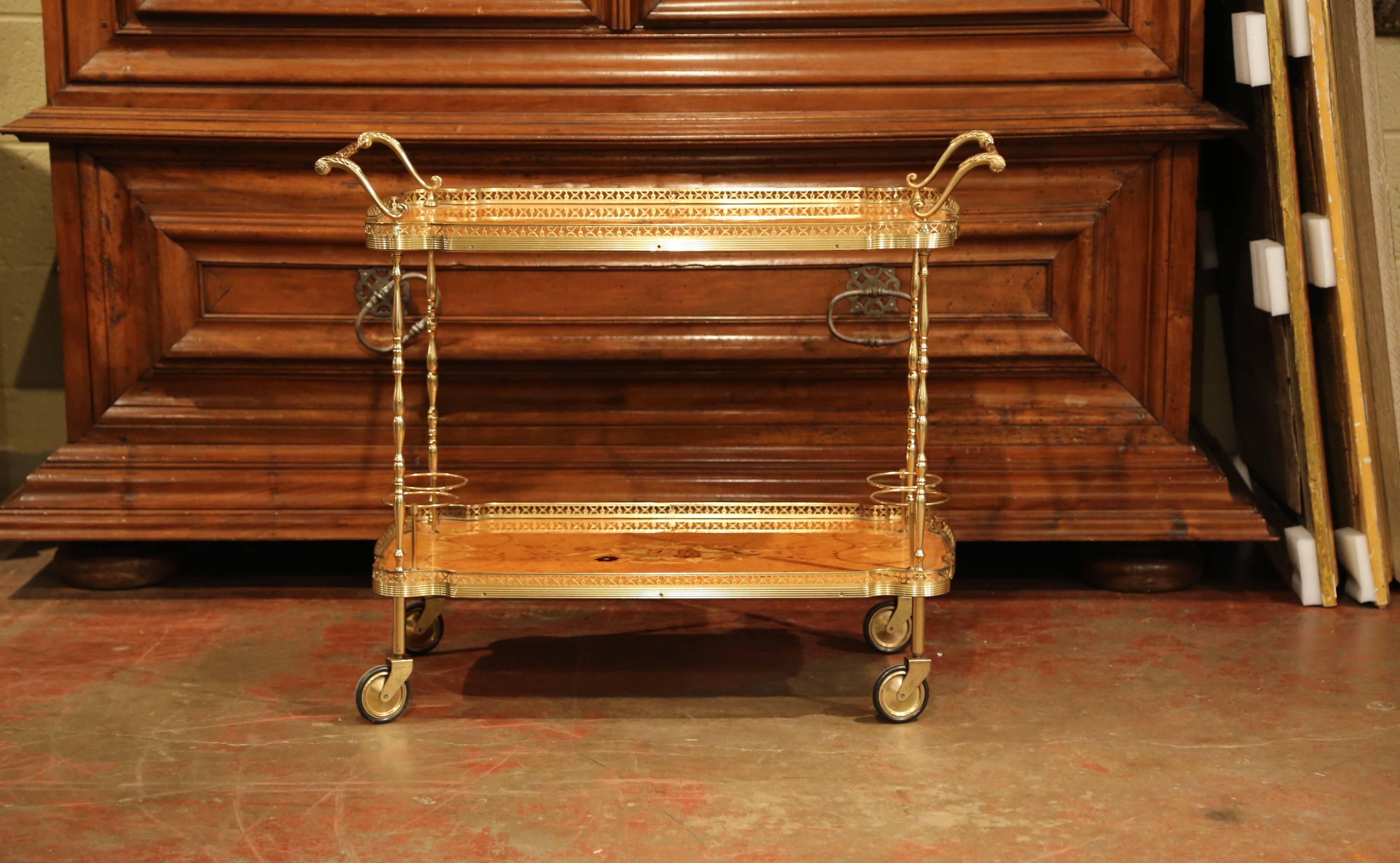This fine wooden and brass cart was created in France, circa 1960. The brass cart sits on four wheels and features large handles on both sides of the top deck. The two decks feature a decorative brass gallery around the perimeter, and both surfaces