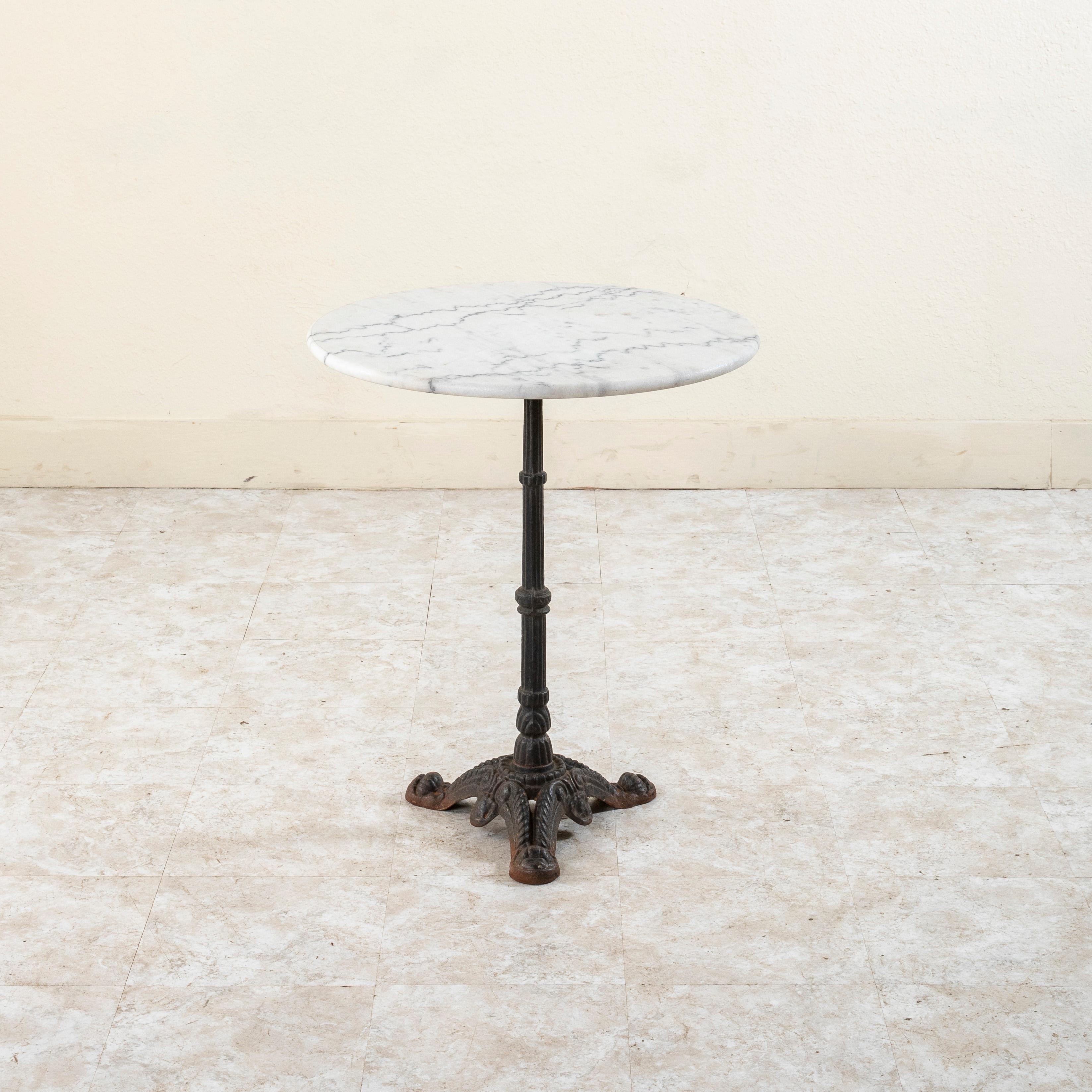 This classic French iron bistro table or cafe table from the mid twentieth century features a round honed white marble 24-inch diameter top with a rounded edge. The top rests on a cast iron base supported by a central fluted pillar. The base is