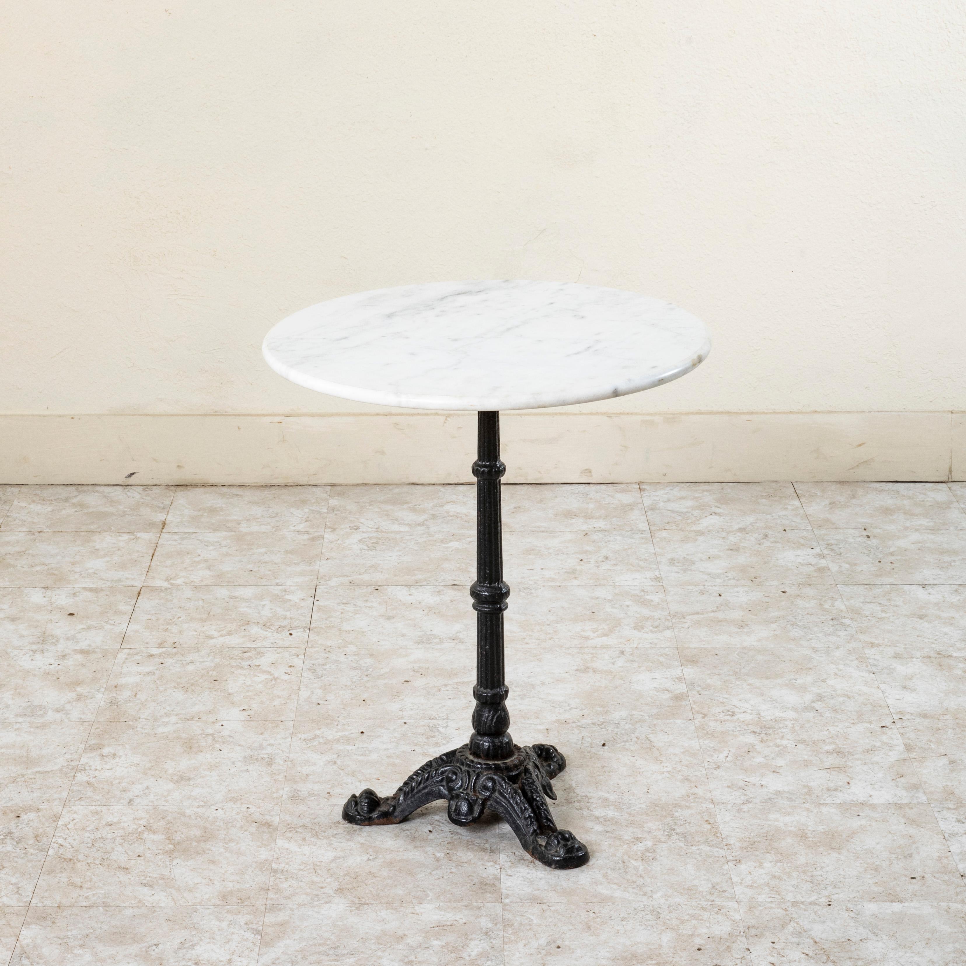 This classic French iron bistro table or cafe table from the mid twentieth century features a round honed white marble 23-inch diameter top with a rounded edge. The top rests on a cast iron base supported by a central fluted pillar. The base is