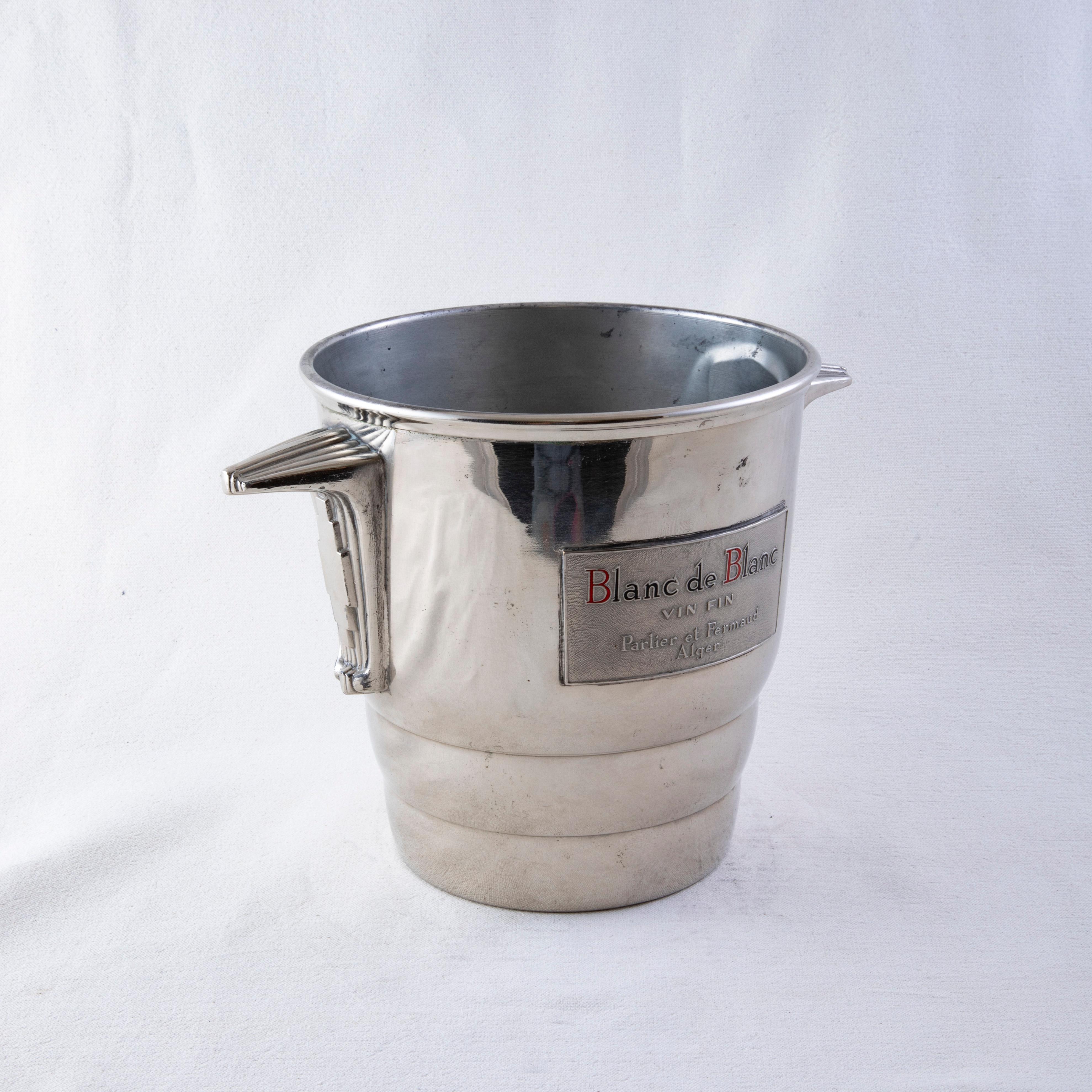 This French silver plate champagne bucket from the mid twentieth century bears the label of the champagne Blanc de Blanc in black and red enameled letters. Below is the name Parlier et Fermaud and the name of the capital city in Algeria. A handle on