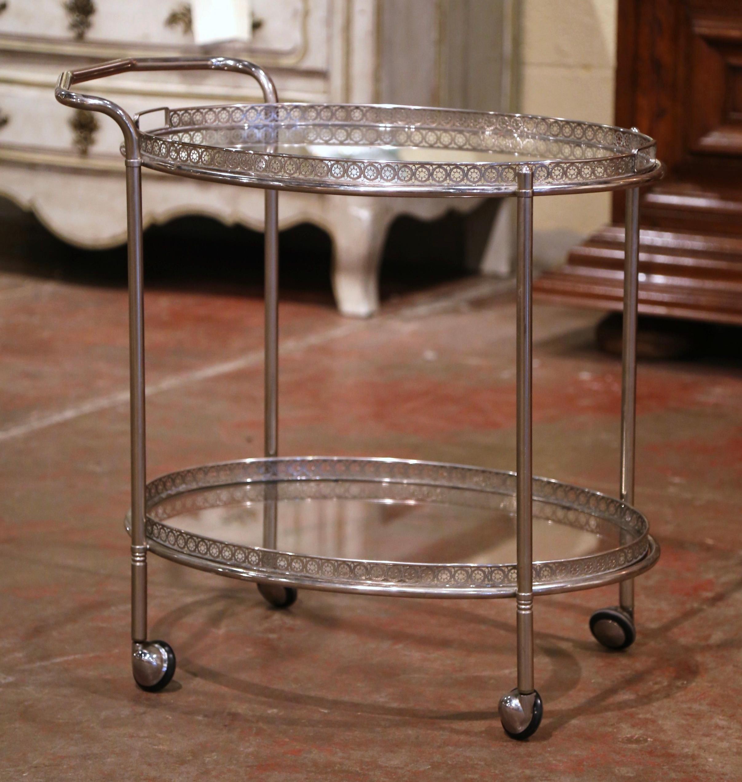 This elegant, vintage rolling bar cart was created in France, circa 1950. The dessert table stands on small casters wheels over straight legs, and features two oval plateaus topped with glass surfaces. The top deck has a shaped utilitarian handle