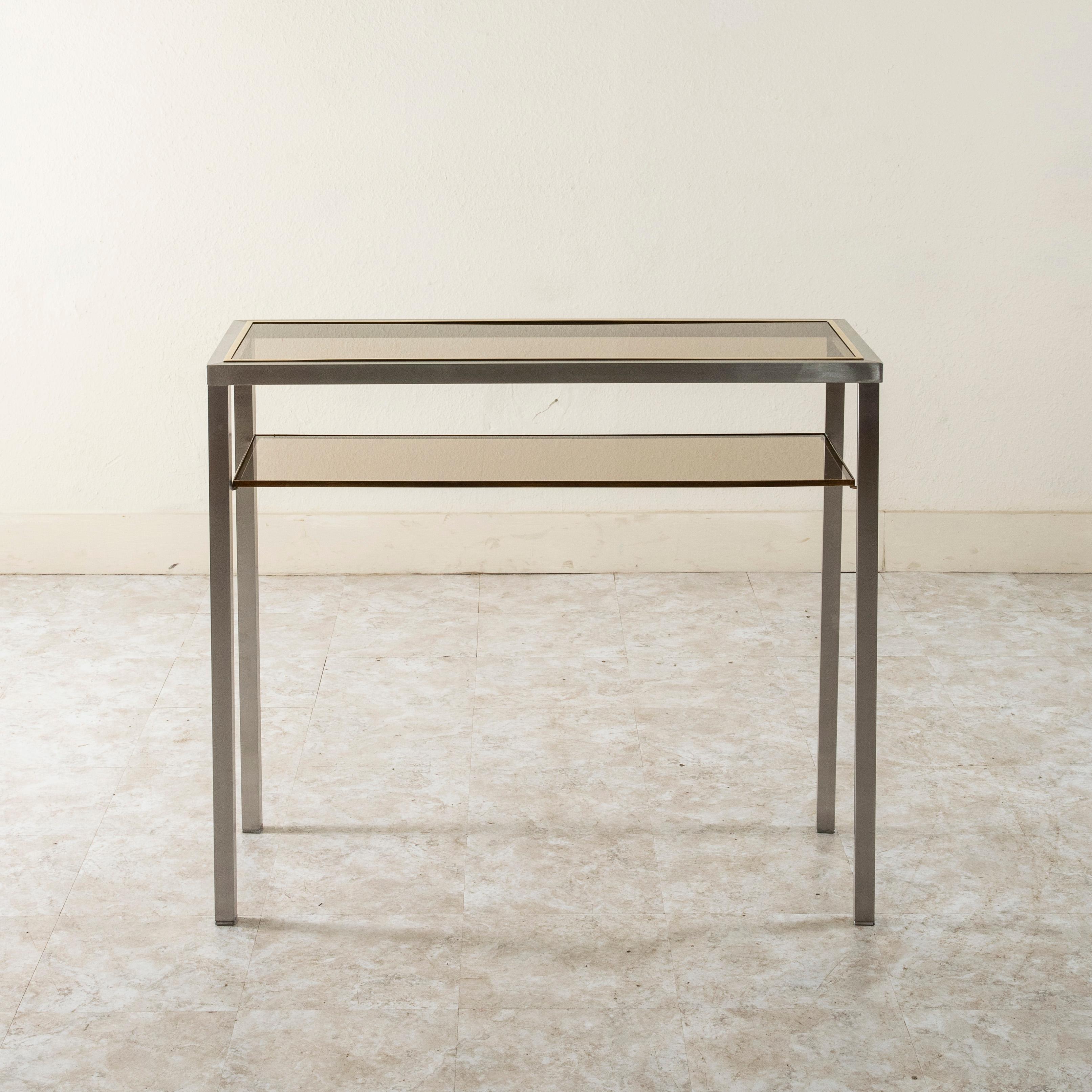 This narrow 14.5 inch deep French mid-century console table or sofa table features a sturdy steel frame and a smoked glass top. Brass trim surrounds the smoked glass on the top and around the lower smoked glass shelf. c. 1960.