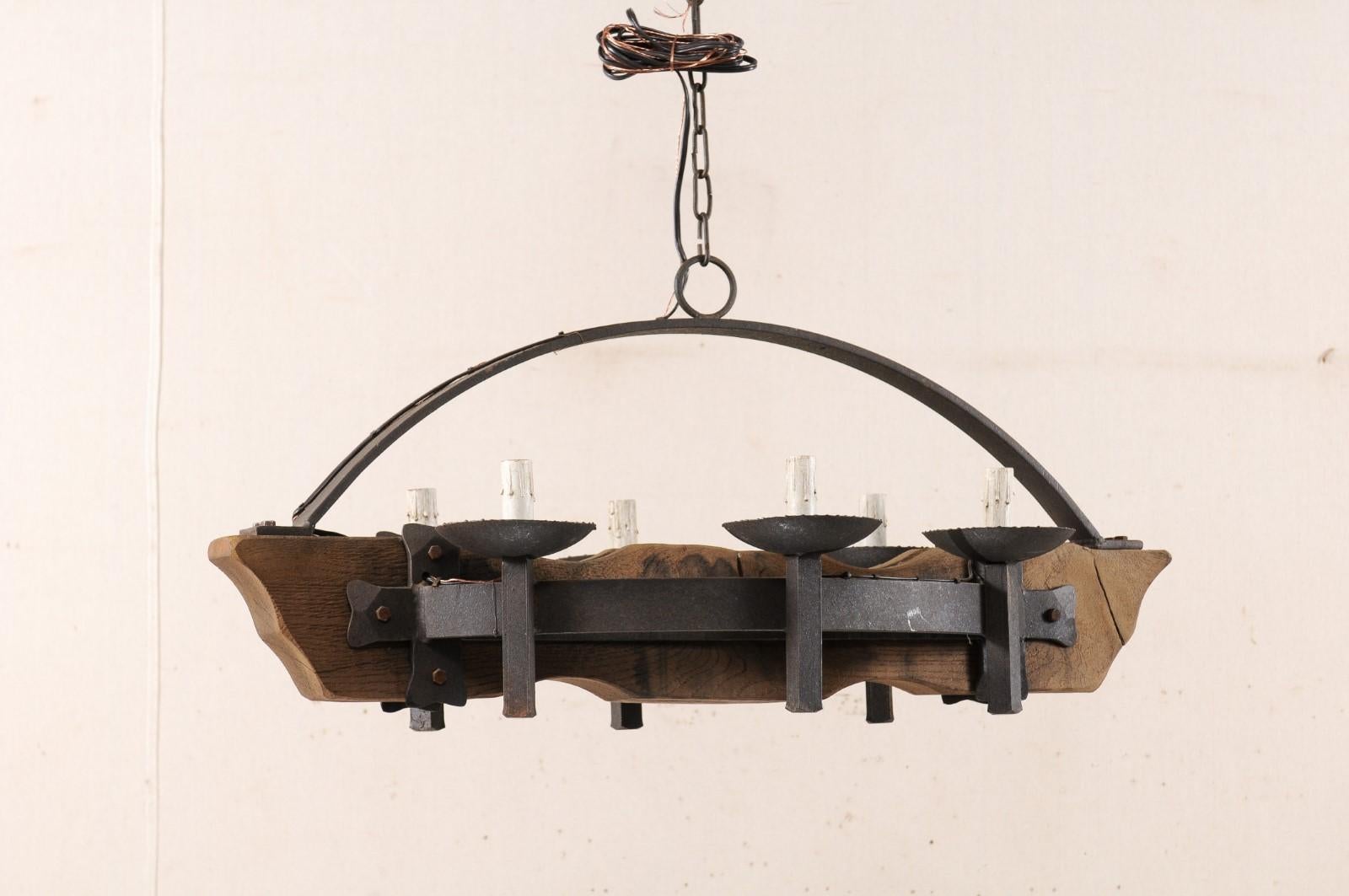 A vintage French six-light wood beam and forged iron chandelier. This mid-20th century chandelier from France features a central wooden beam, from which each long side supports a bowed iron bar with three torch style arms mounted along it's