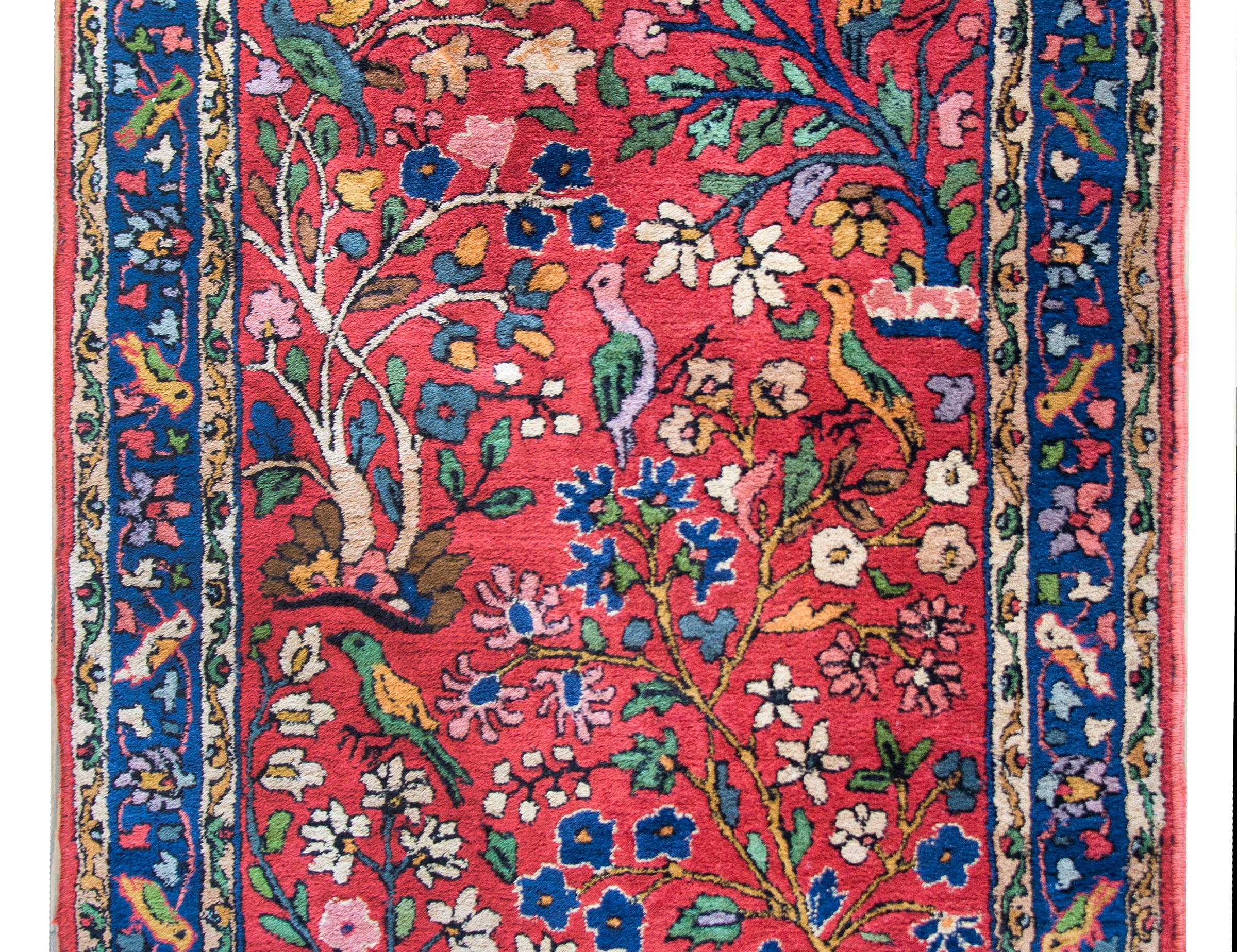 A playful mid-20th century German Tetex rug with an all-over tree-of-life pattern with myriad flowering trees with multi-colored flowers and leaves, and several birds, all set against a crimson background, and surrounded by a wide border with