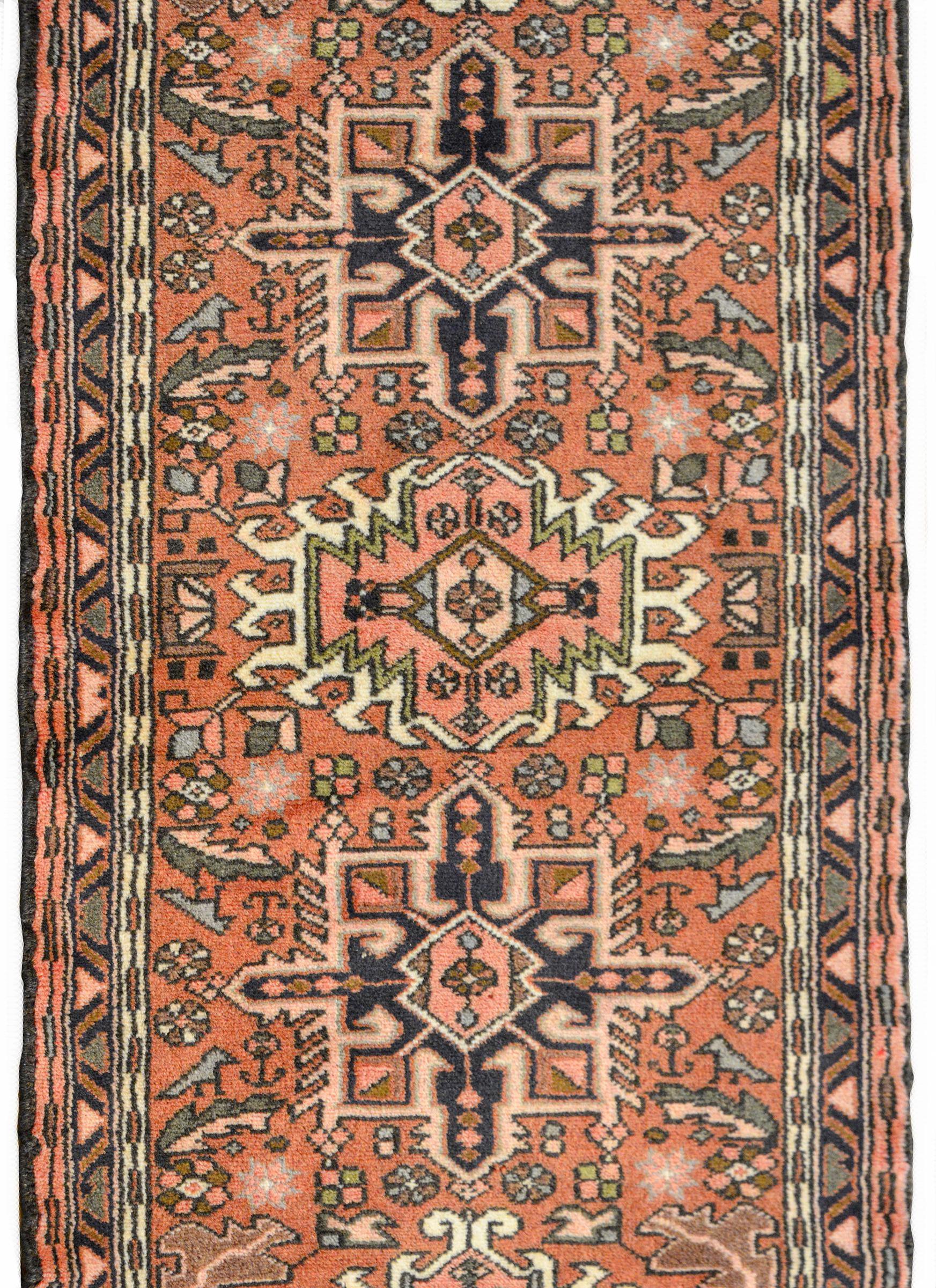A wonderful mid-20th century Persian Karadja runner with several stylized floral medallions woven in black, pink, light blue, and gold amidst a field of more stylized flowers against a muted crimson background. The border is wonderful composed with