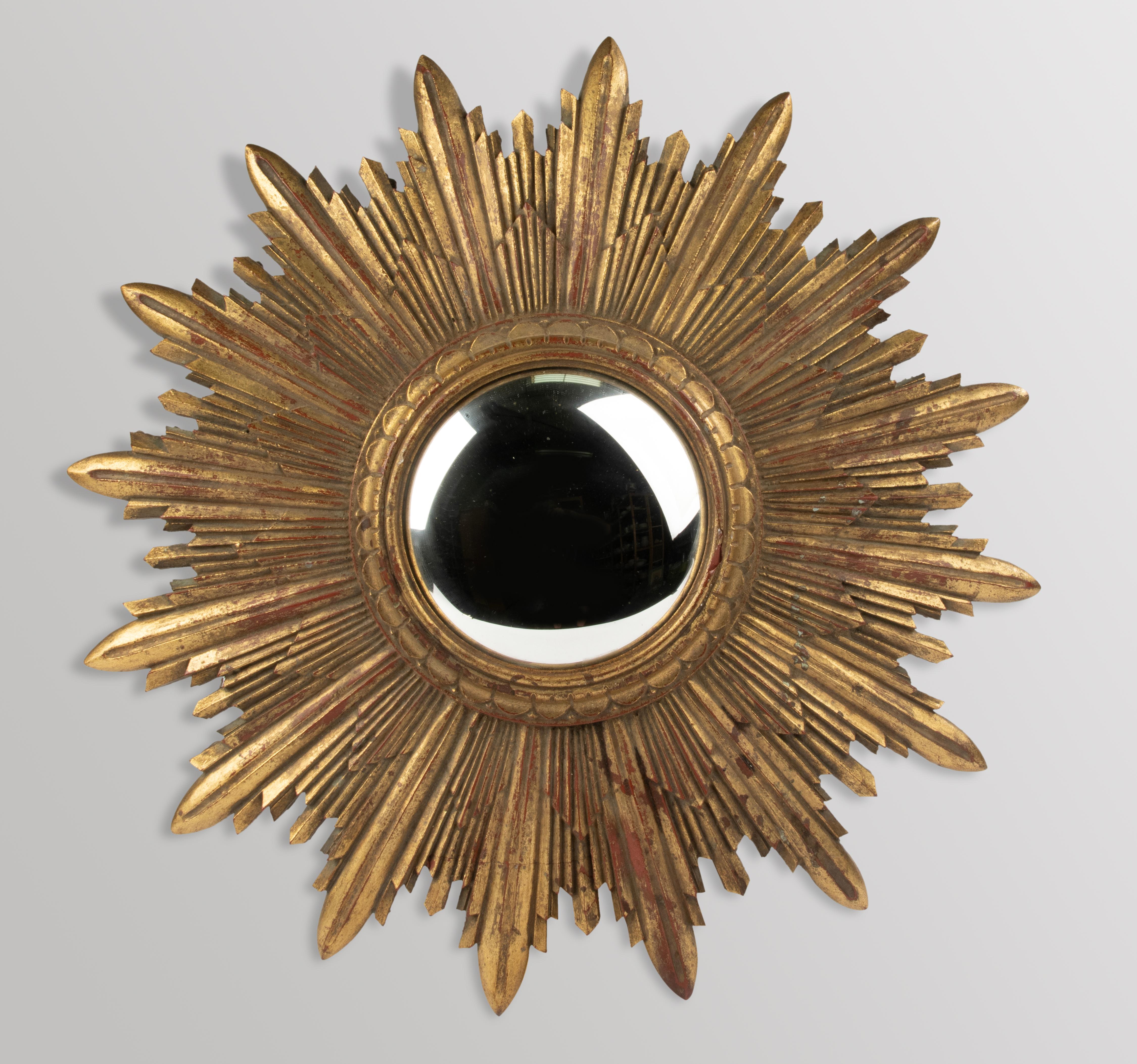 A striking sunburst mirror made in Belgium circa 1960, featuring a bold and sculptural form with beautiful gilded surface and rich patina. The frame is crafted from resin, cast in deeply layered rays that radiate dramatically around the central