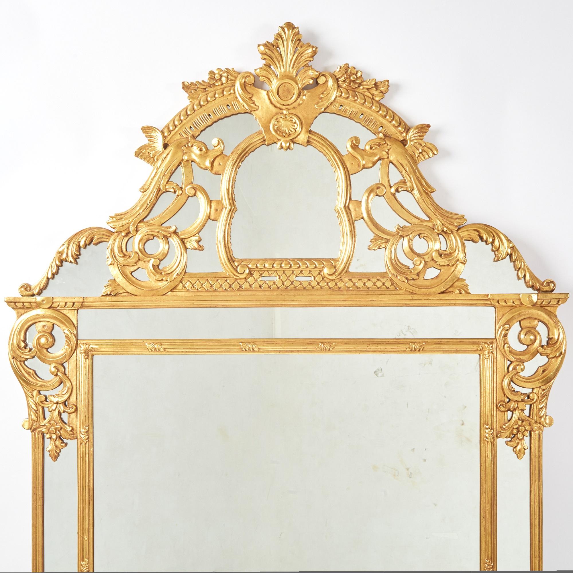 Questo magnifico specchio da parete in stile Regency della metà del XX secolo è un vero capolavoro di artigianato italiano. Caratterizzato da un'imponente dimensione, lo specchio è ornato da dettagli in legno dorato intricatamente intagliati, che