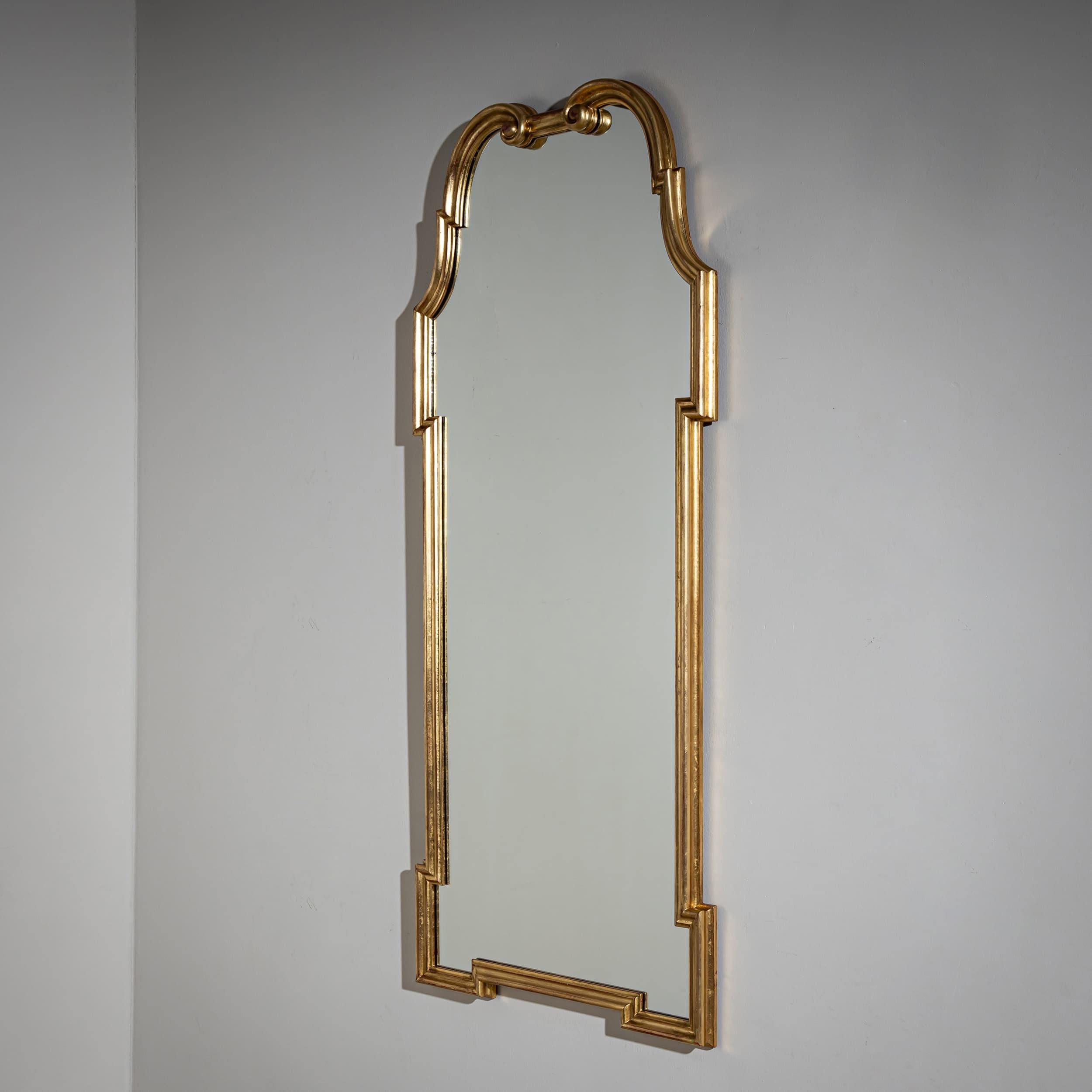 Wall mirror from the mid-20th century in a gold-patinated, profiled frame. The mirror is rounded and shows volute elements in the upper area. Stamped on the back: Palladio - Made in Italy.