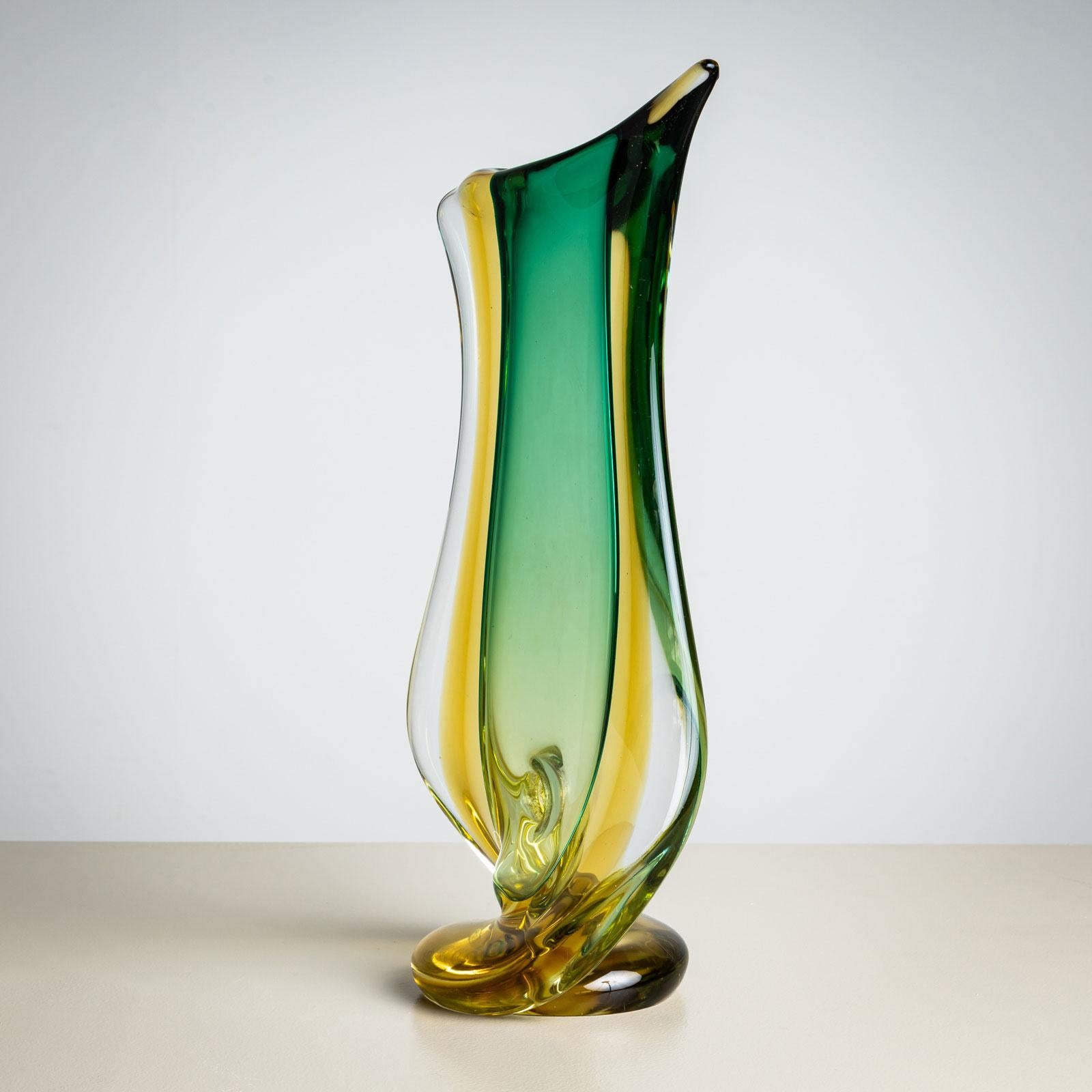 An extraordinary glass vase by Seguso Vetri d’Arte, crafted in Italy in the mid-20th century. Made of clear glass with green and yellow inclusions, the vase stands on a round base. Its asymmetrical form, reminiscent of a fish tail, gives it a