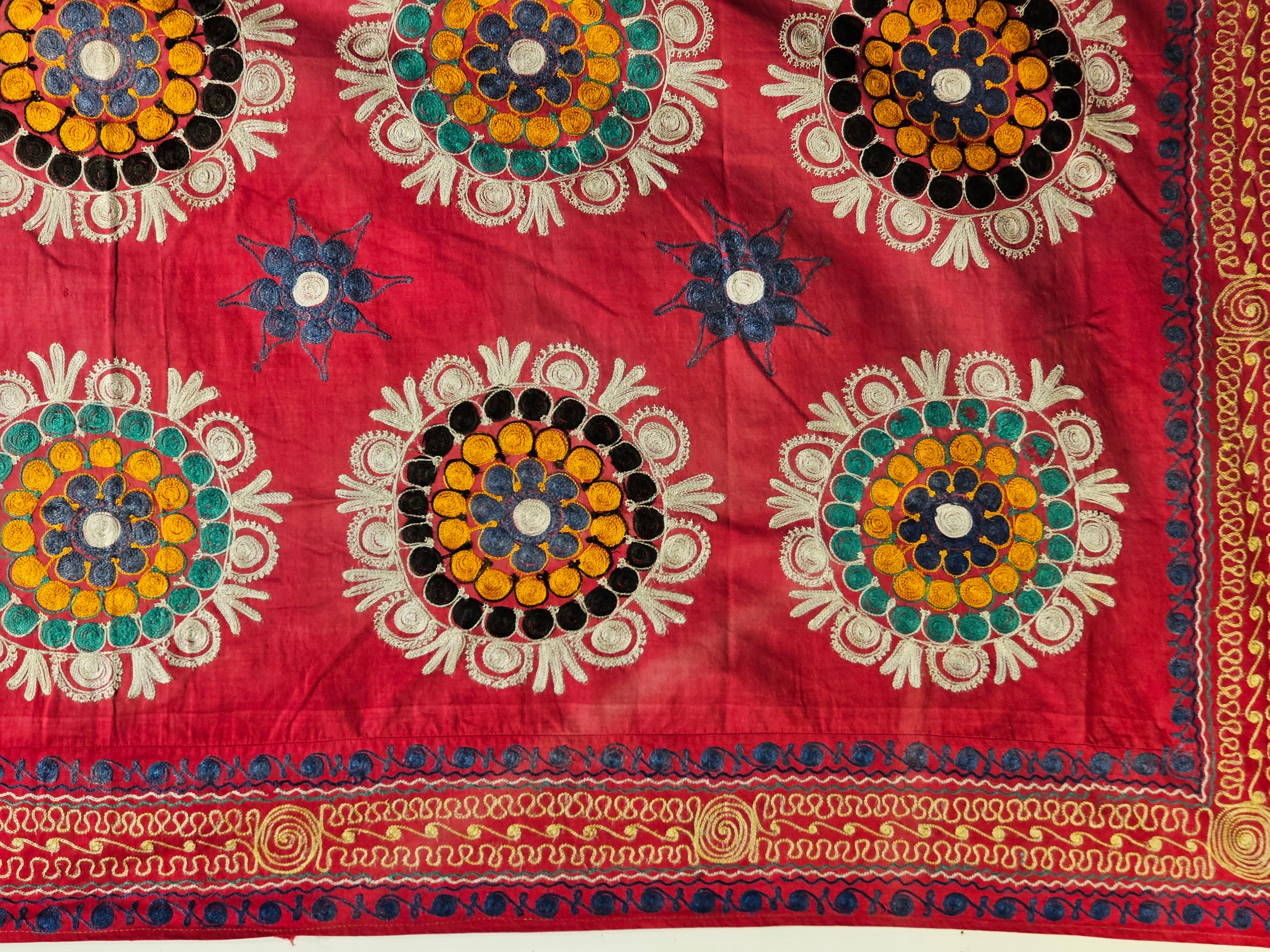 A Vintage hand crafted Silk Suzani Embroidery in medallion design from Uzbekistan in Central Asia circa the 3rd quarter of the 1900s.  This Suzani Embroidery depicts three columns of round embroidered medallions each with a different color scheme.