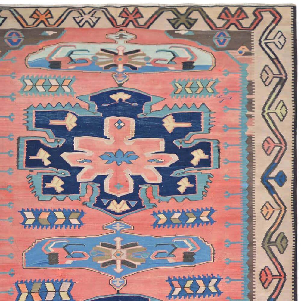 This handwoven Kilim comes from the Caucasus and is made of durable, but soft, textured wool. The ornaments in the middle are surrounded by strong symbols in red shades, which resemble a tribal geometry, and reinforced by a deep dark blue