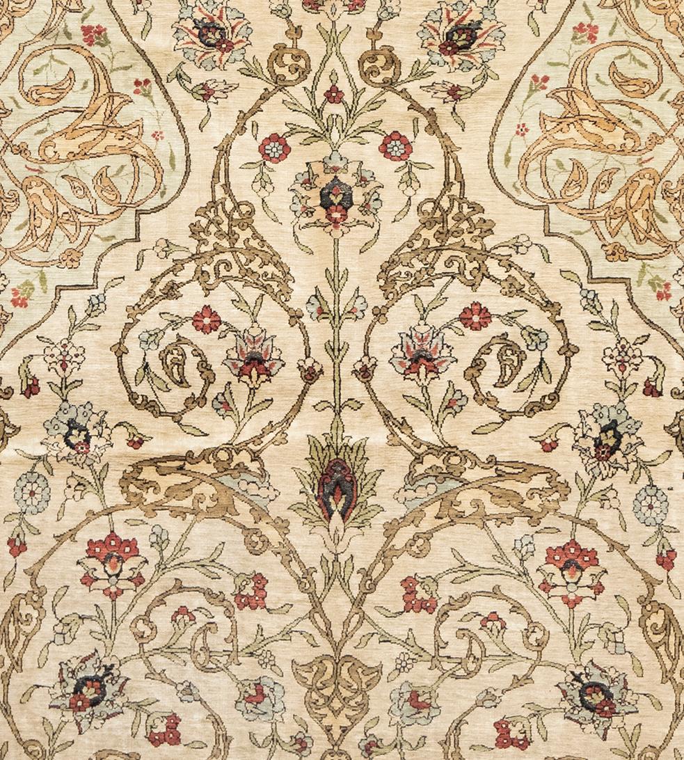 This silk Hereke rug has an ivory field with a scrolling palmette and floral vine, cusped light blue mihrab arch above containing scrolling arabesque vine, the light blue spandrels similar, in broad brick-red border of meandering palmette split