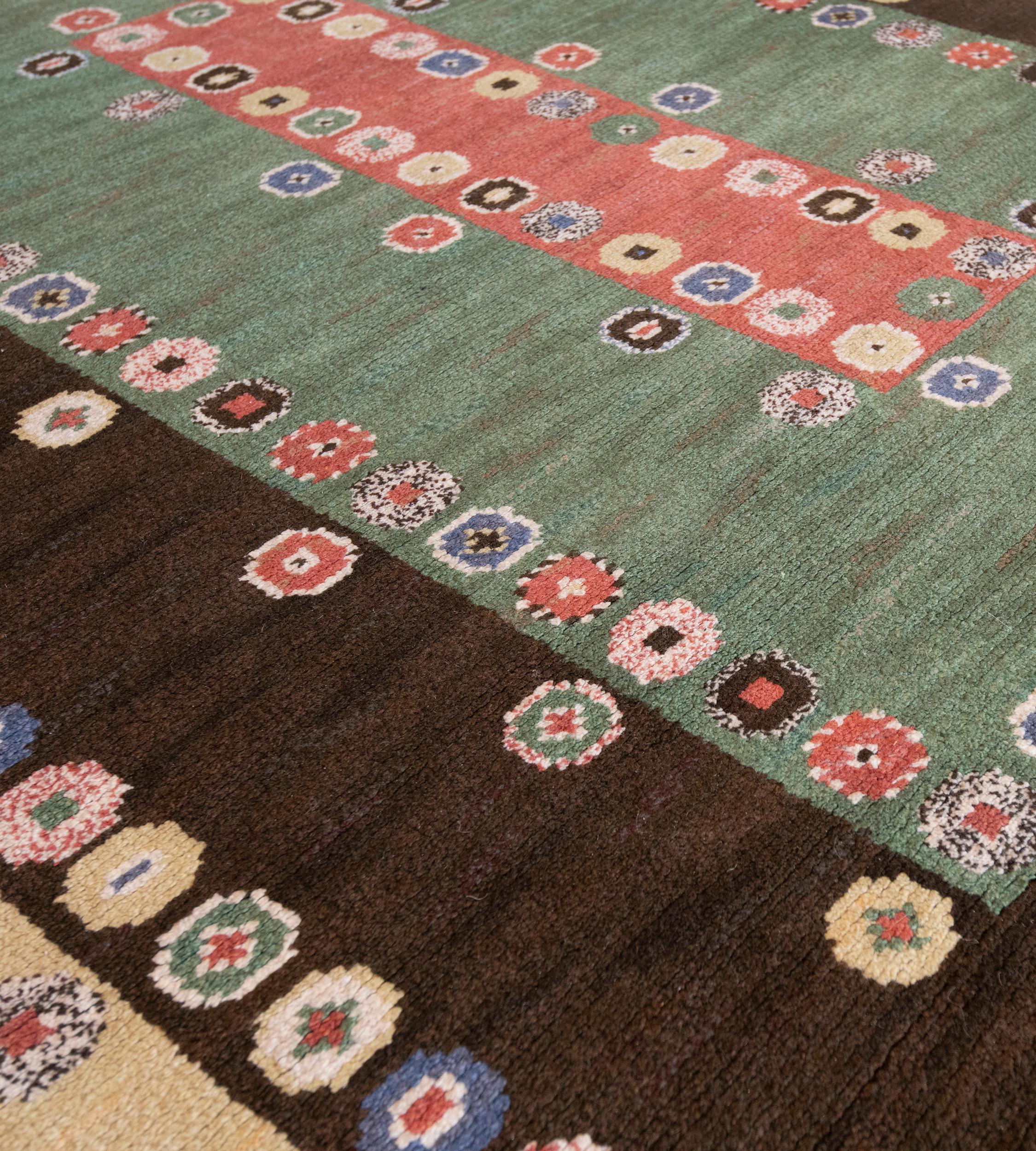 This signed Swedish rug has a chocolate-brown field with an outer band of polychrome octogen lozenges and a similar spaced band of lozenges around a moss-green rectangular panel with outer and inner rows of polychrome lozenges around a shaded red