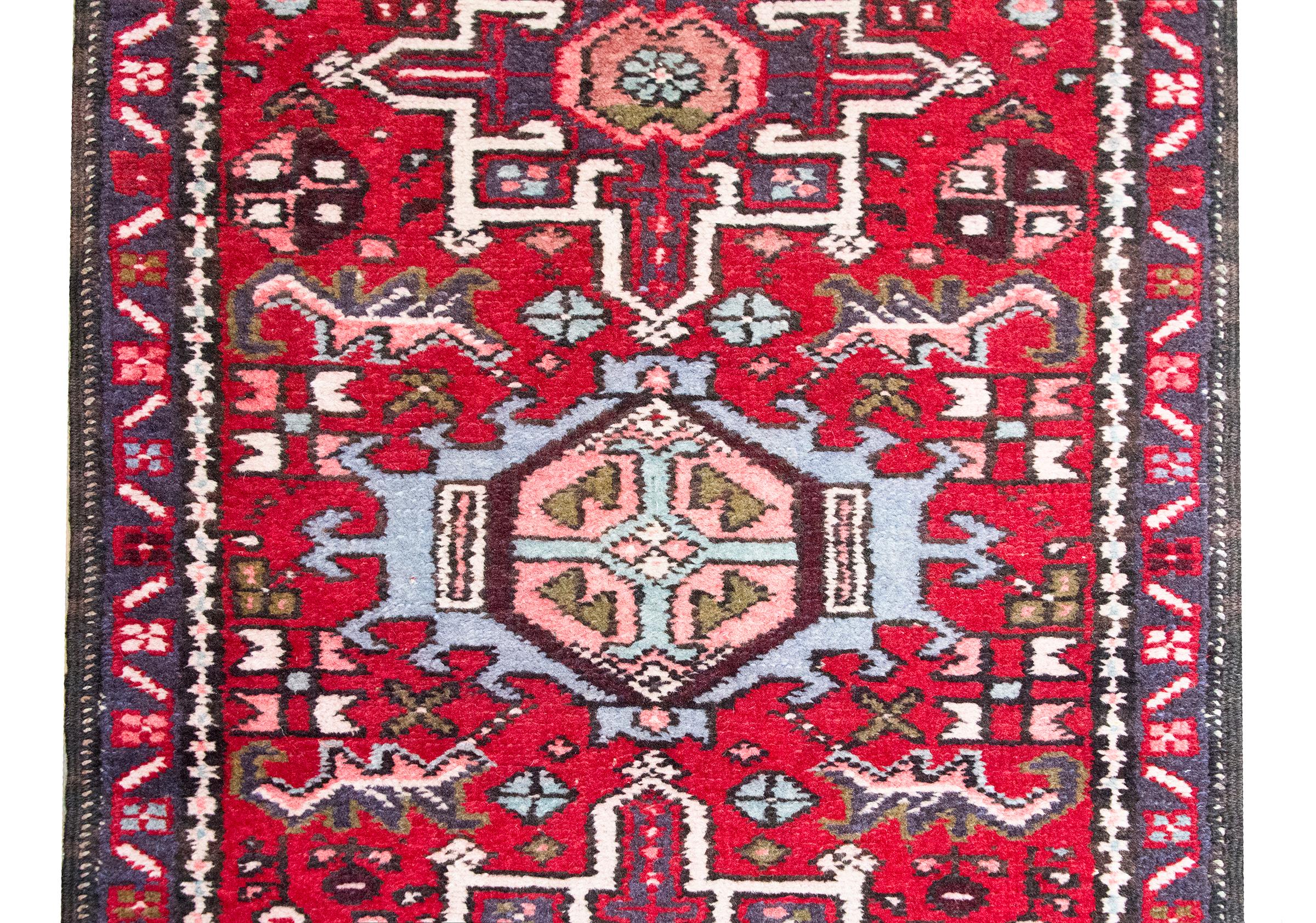 This mid-20th century Persian Heriz runner features a dynamic series of stylized floral medallions running its length, each set within a richly patterned field of scrolling vines, leafy tendrils, and geometric blossoms. Woven in a lively palette of