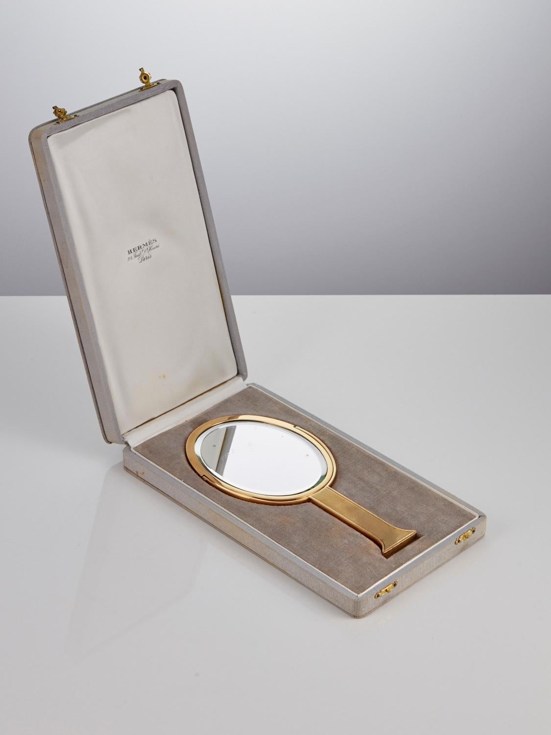 Miroir à main Hermès du milieu du 20e siècle, en boîte, en argent doré, marqué Paris et daté Circa 1950.

Ce charmant et élégant miroir à main Hermès possède un verre biseauté pivotant, un côté plat, l'autre grossissant. 
La plaque présente