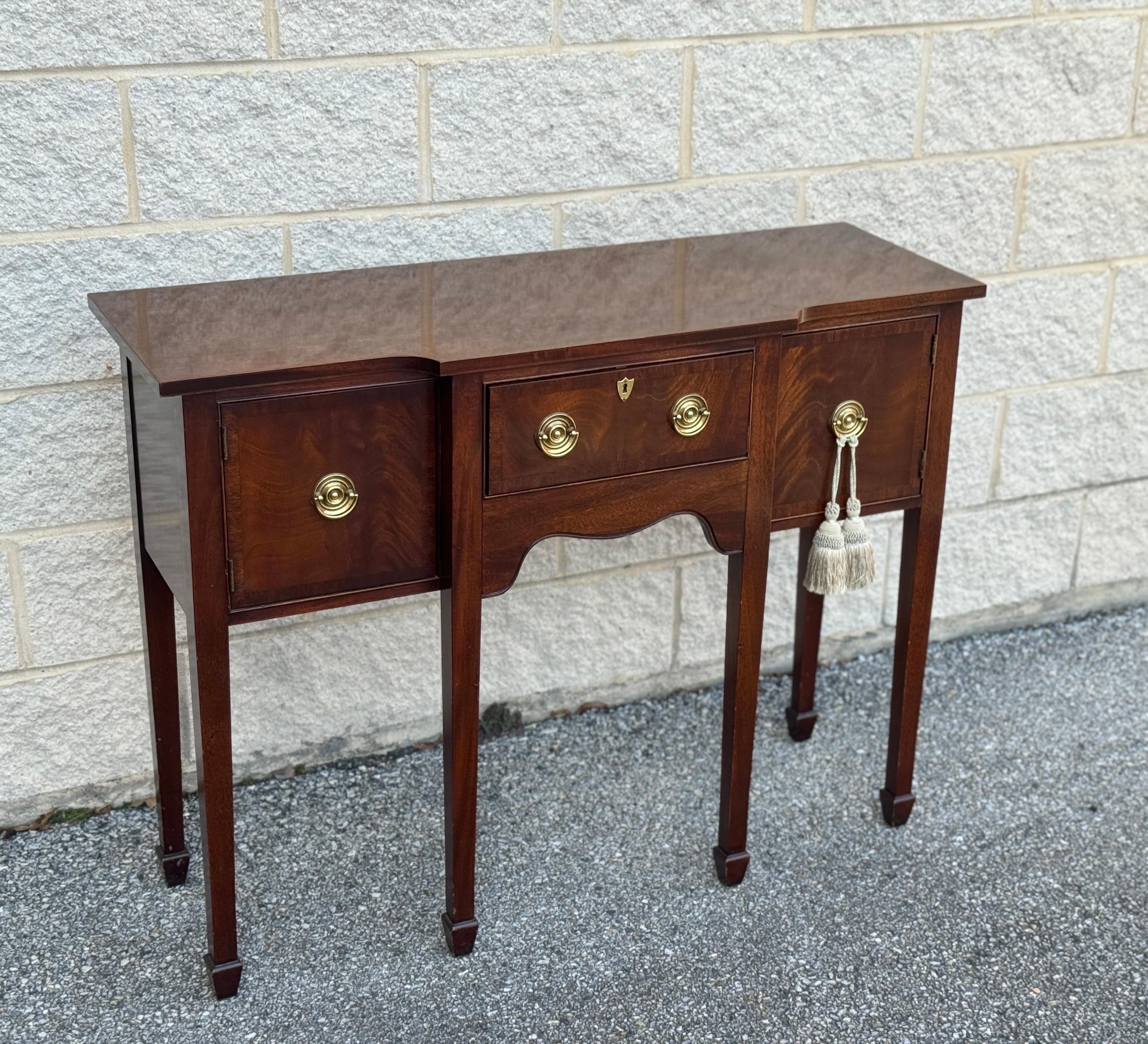 Small console table by Hickory chair company. Features two side compartments with doors and a central drawer. Brass details.