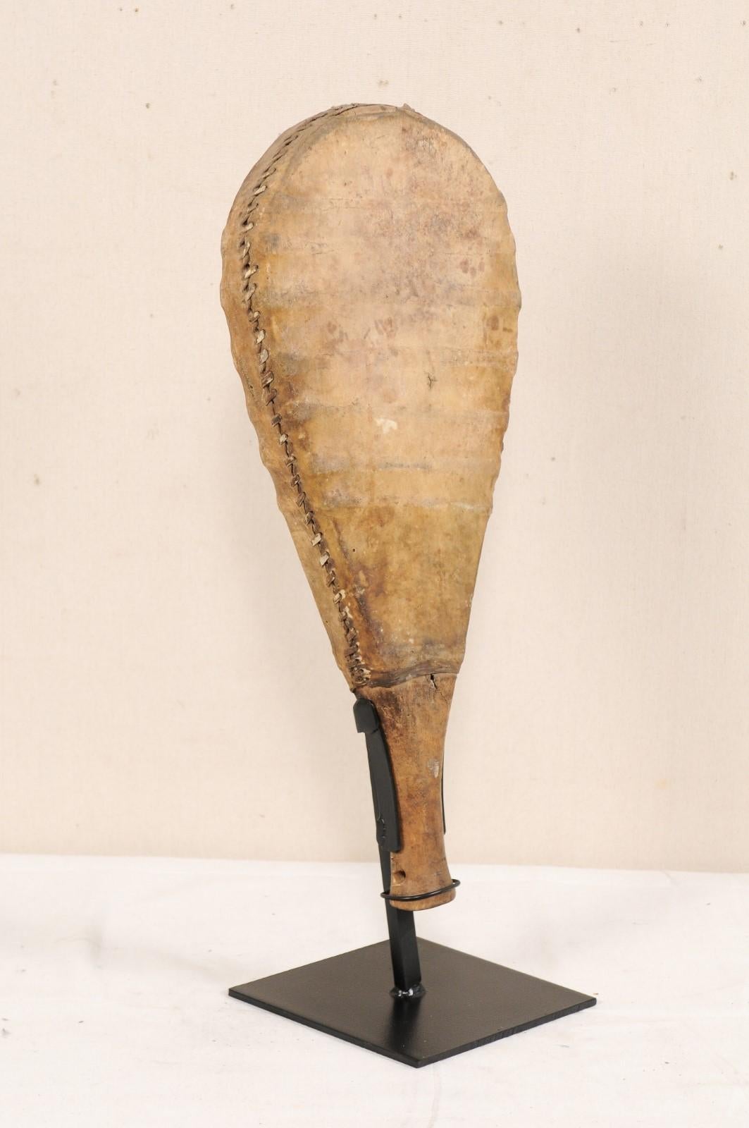 A leather and wooden gaming paddle from the mid-20th century. This vintage game paddle from India features a wooden handle and droplet-shaped body which has been wrapped in stretched leather and handstitched along it's sides. The paddle has been