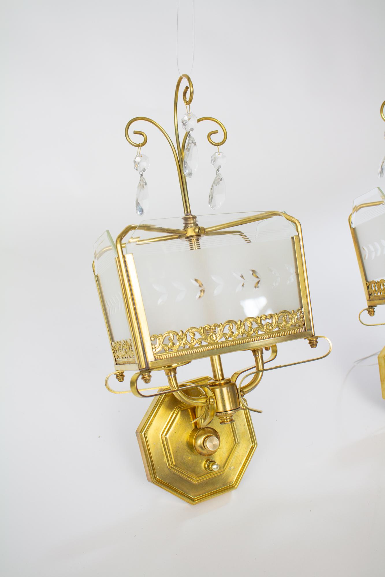 Mid 20th Century hollywood regency etched glass panel and brass sconces. Etched and Frosted glass panels with beveled edges on the front and sides held in place with a brass frame. Delicate brass curls from top and holds crystals. Two lights.