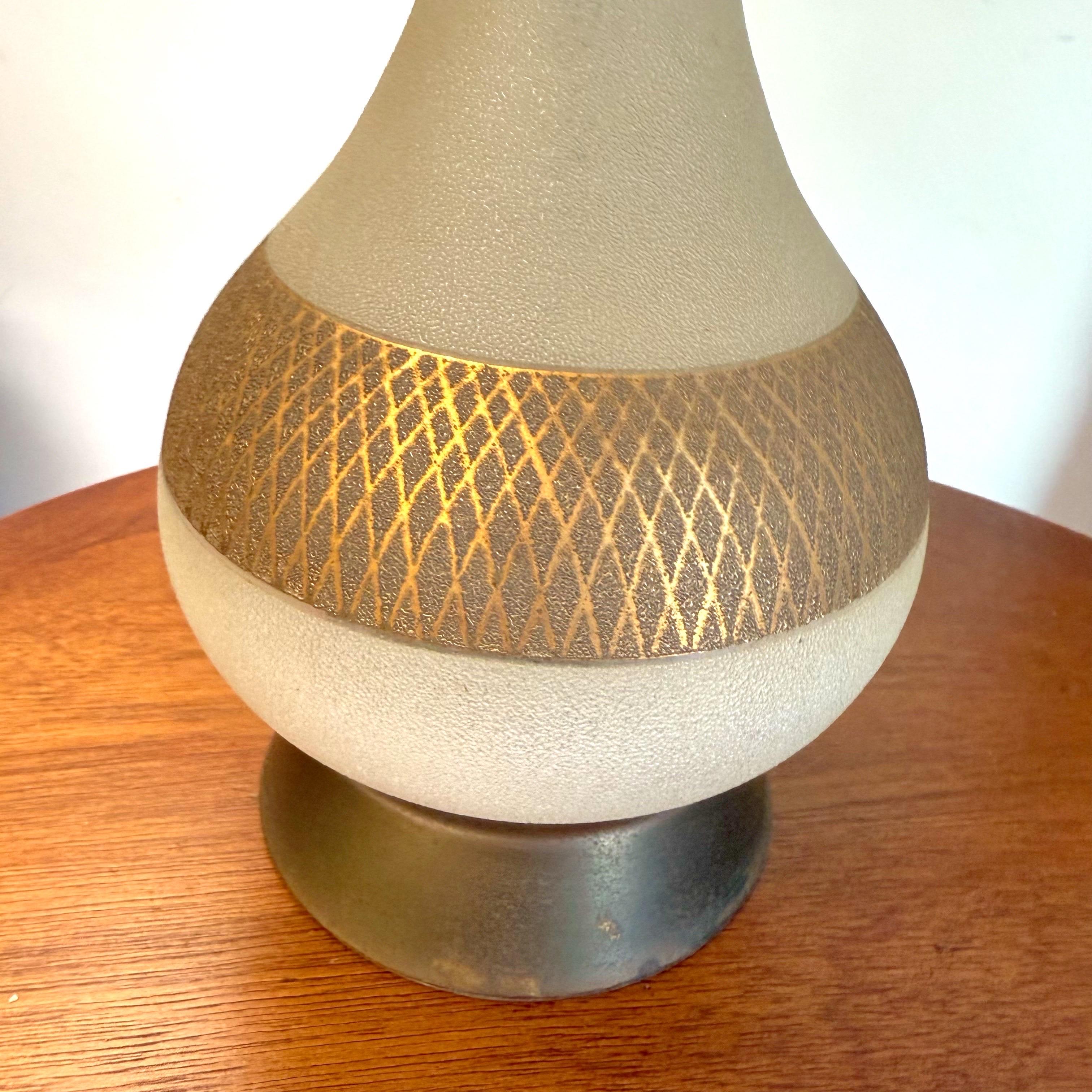 Eine glamouröse Hollywood-Regency-Tischlampe aus der Mitte des 20. Jahrhunderts mit einem eleganten Milchglaskörper und vergoldeten Details. Die vasenförmige Form ist mit einem strukturierten goldenen Rautenmuster akzentuiert, das auf einem Sockel