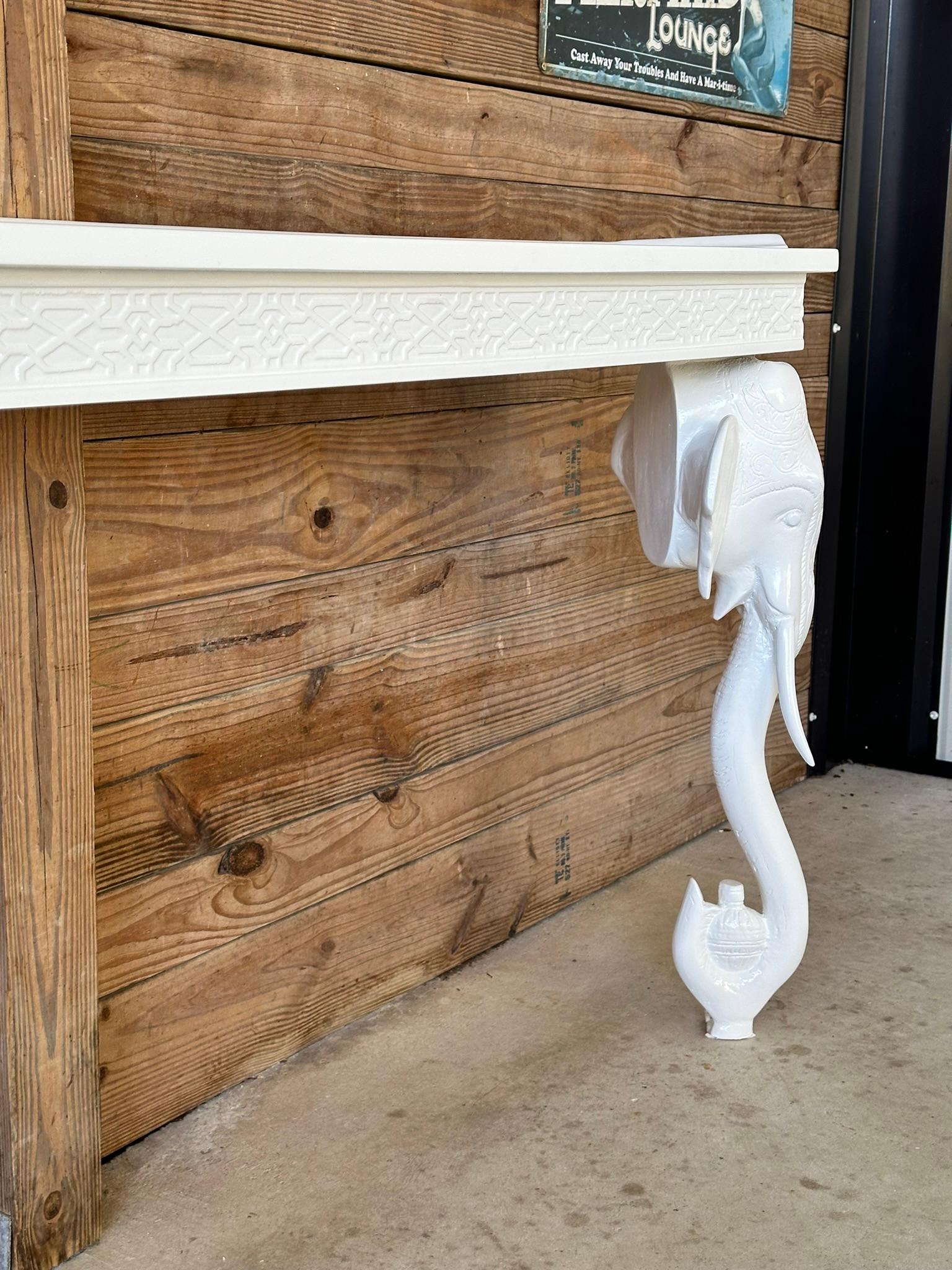 Te presentamos una consola de pared vintage restaurada de elefante tallado lacado en blanco de Gampel-Stoll, perfecta para añadir un toque de estilo Hollywood Regency a tu decoración. Esta exquisita pieza presenta intrincados motivos de elefantes
