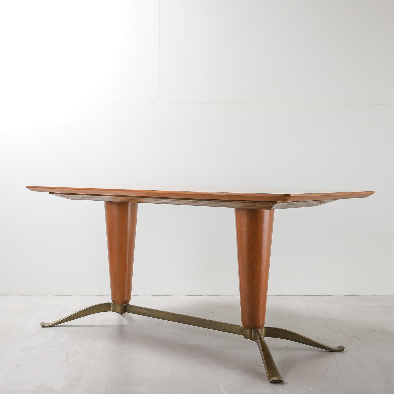 A dining table in bright, honey tone wood, circa mid-20th century, with a table top featuring a starburst pattern at its centre, sitting on two inverted conical pedestals. Four brass feet with stretcher extend from the pedestals. Attributed to Paolo