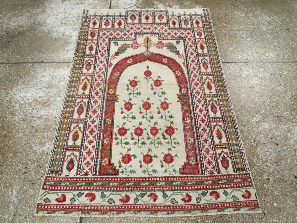 Alfombra de algodón indio Agra vintage. Un arco apuntado columnar encierra trece plantas con flores idénticas y se encaja a su vez en un pórtico escalonado delineado con cruces y cipreses en paneles. La paleta, aunque principalmente marfil, es