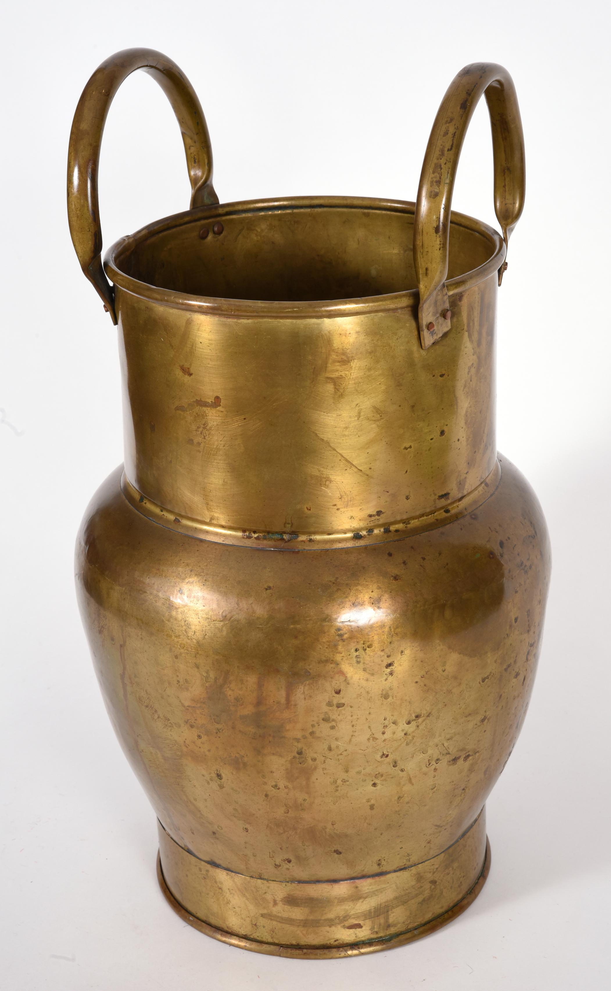 Mid-20th century indoor / outdoor brass umbrella stand or cane stand with two side handles. The umbrella stand is in good used condition. The umbrella stand measure about 19.5 inches high x 10.5 body diameter x 8 inches base diameter.