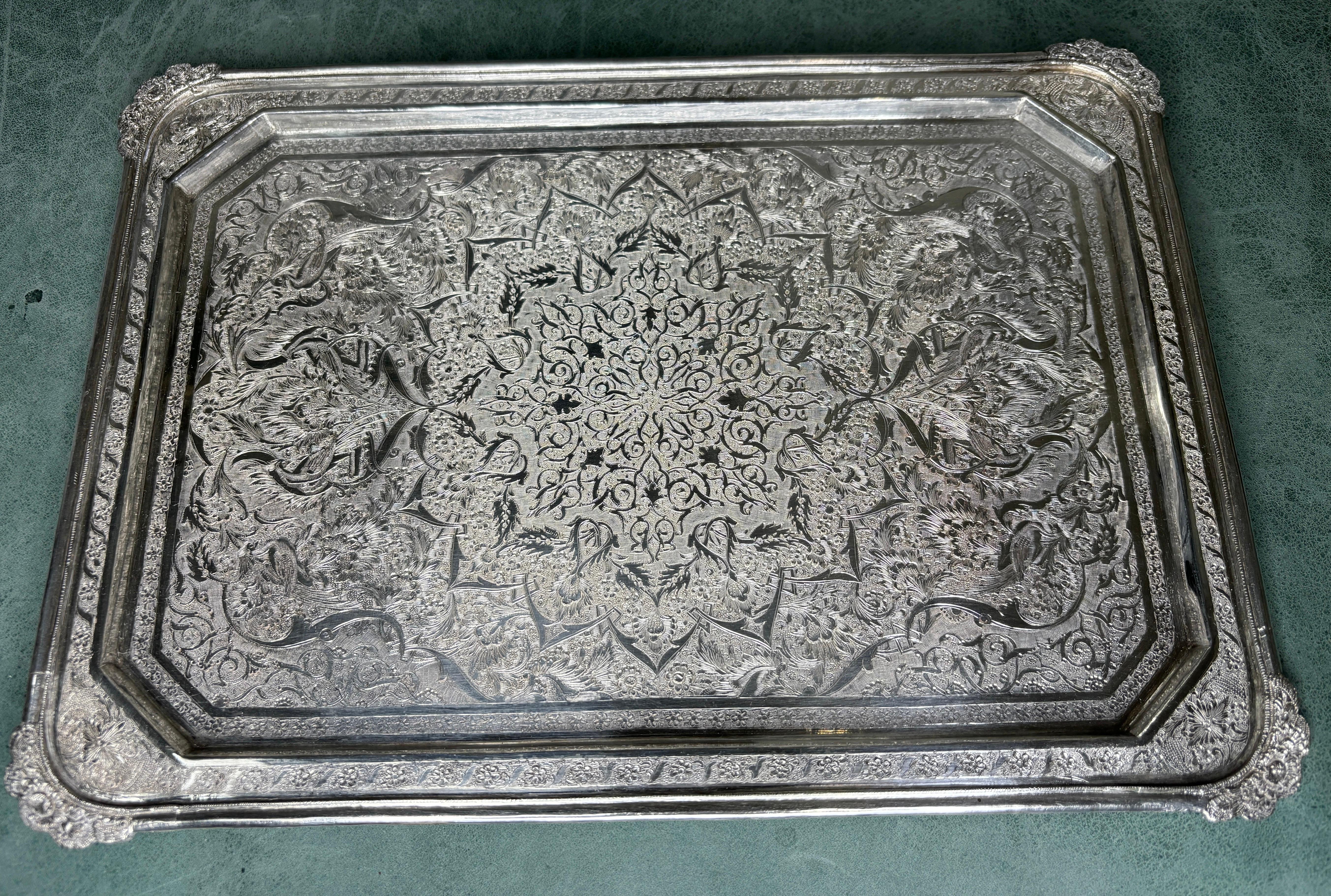Persian silver tray with rounded corners.  Imbued with intricate craftsmanship and adorned with delicate bird and foliate patterns, this silver tray is a masterpiece that will elevate your silver collection to new heights. 

Its gleaming surface