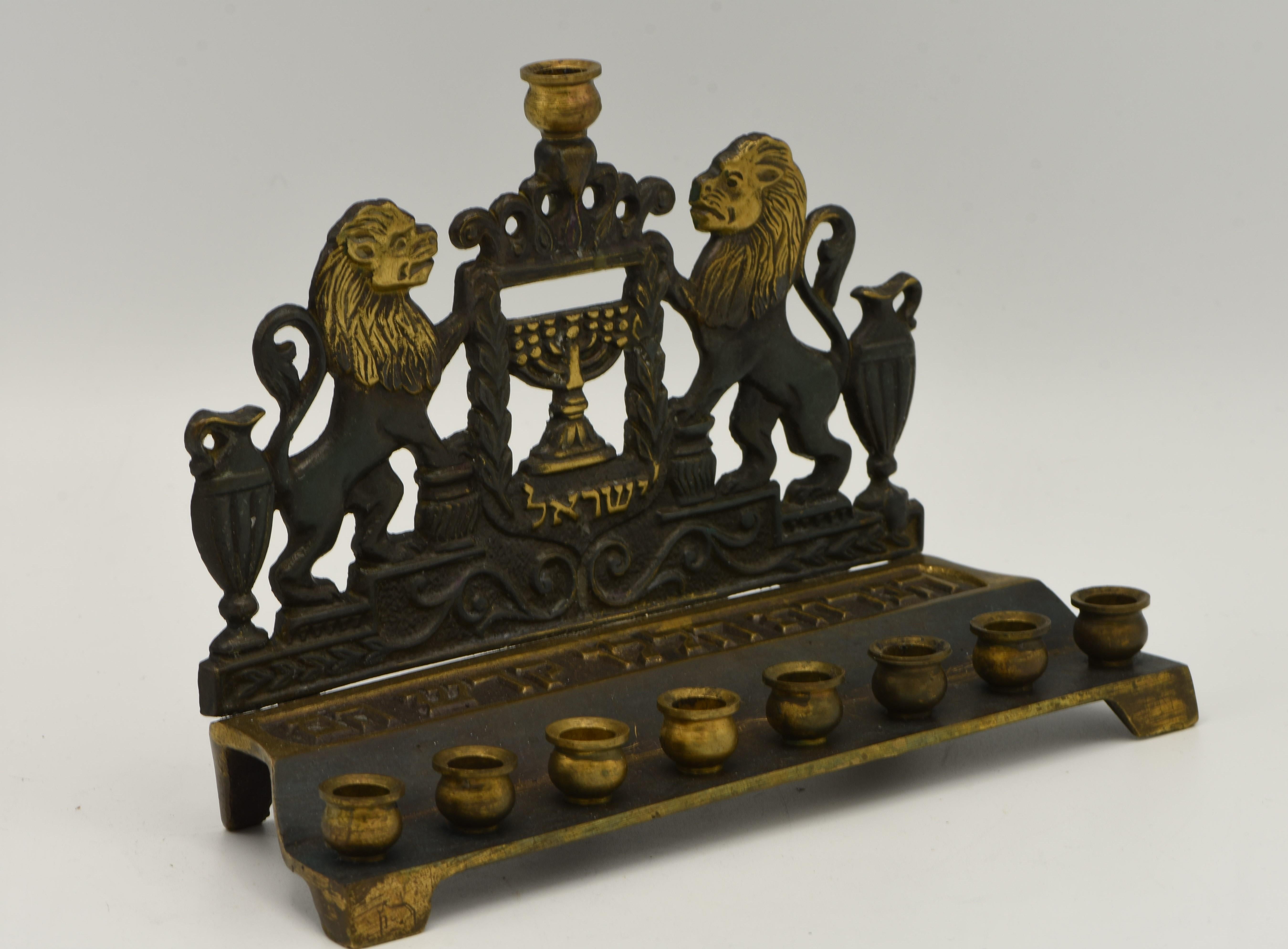 Cast brass Hanukkah lamp menorah, Israel, circa 1950. 
In a green patina finish. The Hanukkah lamp depicts two lions with two oil jugs holding the state of Israel symbol, seven branch menorah with olive branches. Marked on the bottom 