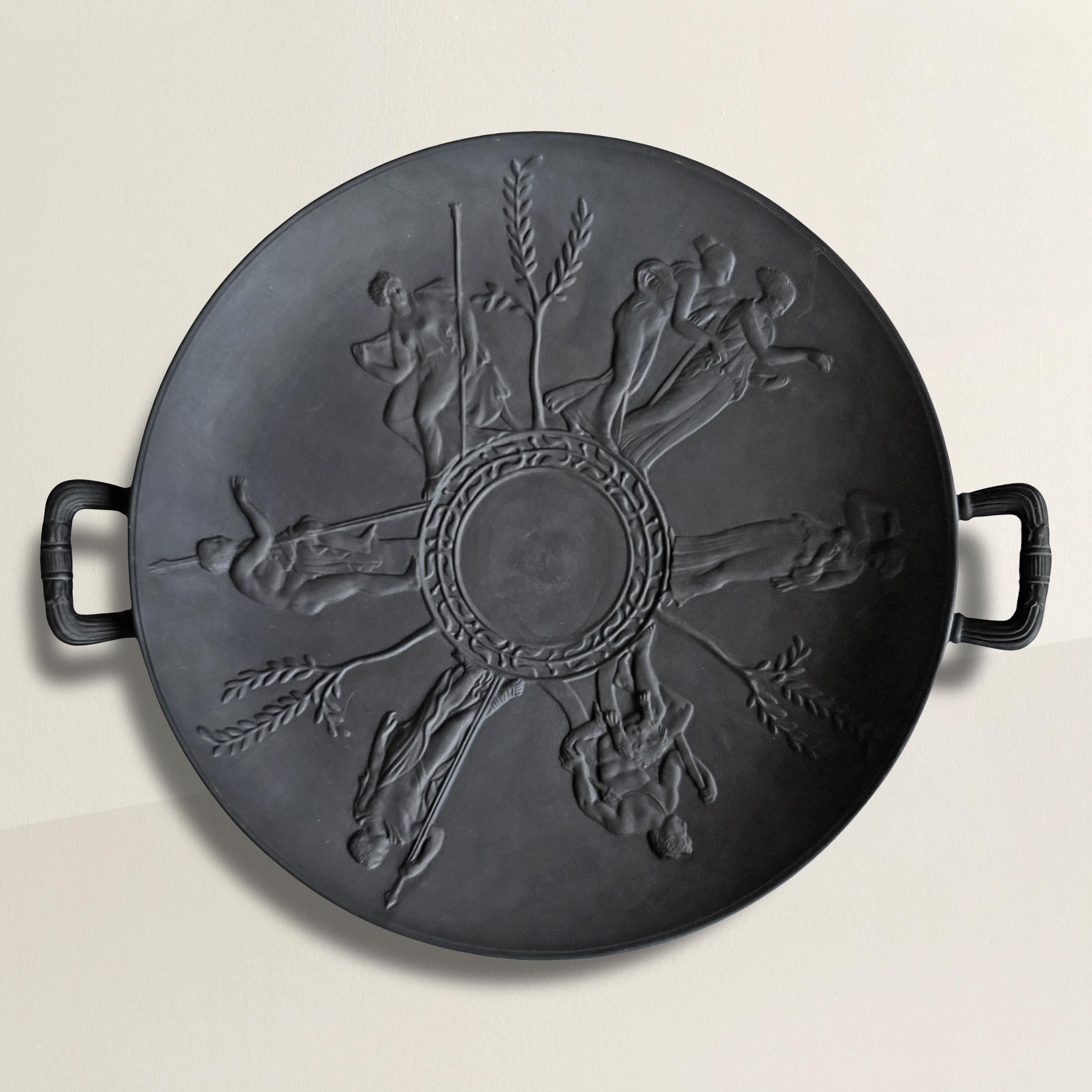 Questa tazza in porcellana di basalto della metà del XX secolo è un raffinato studio di eleganza classica. Con una ciotola larga e bassa, graziosamente sollevata da un piede tornito, le sue proporzioni richiamano la bellezza senza tempo dell'antico