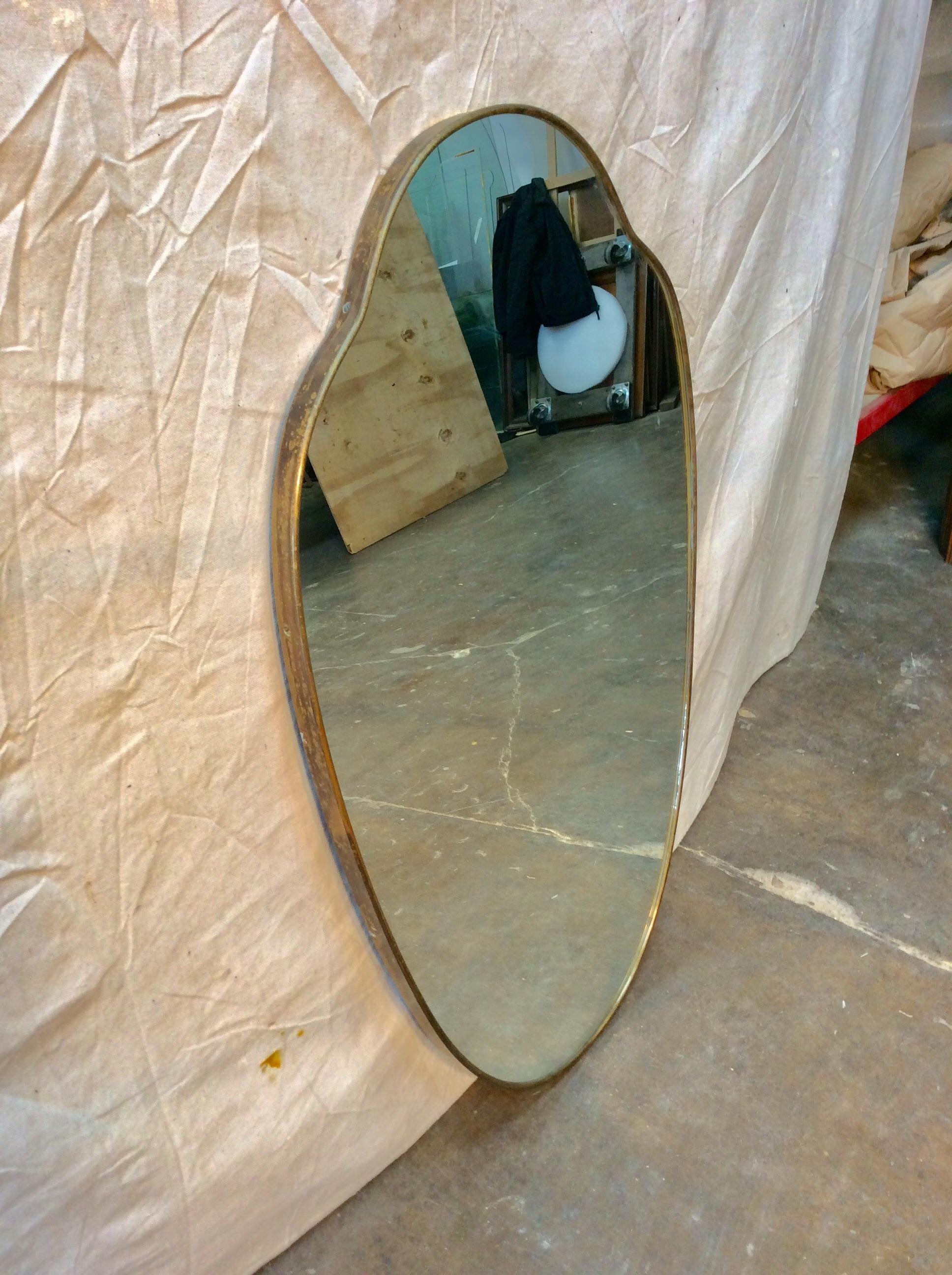 Found in Italy this Mid-20th Century Italian Brass Mirror has a beautiful shield shape and a brass frame. The aged brass frame has a lovely patina but could be polished to sparkle. The piece is in good condition with minor mirror loss and ready to