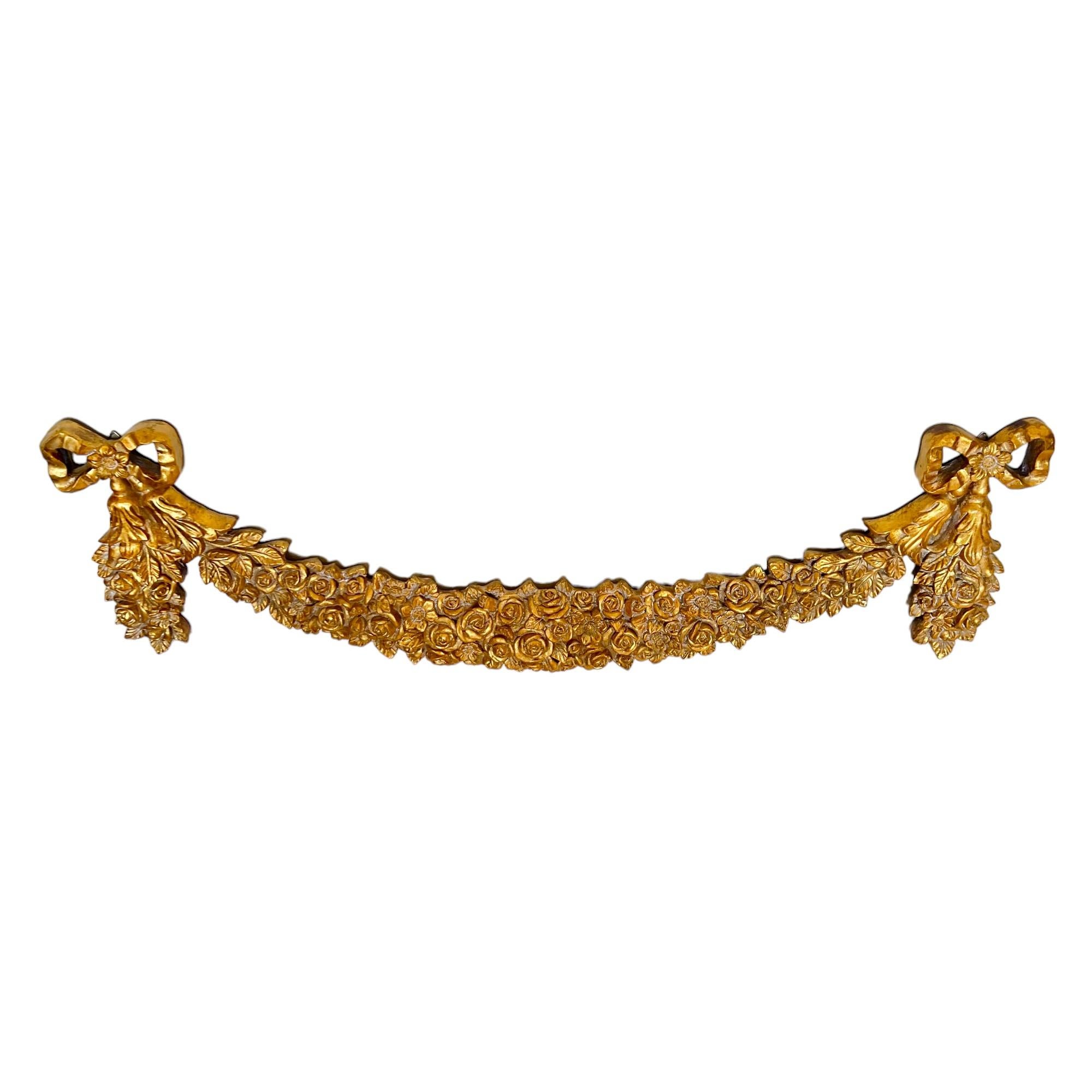 This exceptional Hollywood Regency style Italian gold gilt wall swag or festoon decoration features a floral and foliate motif strung between two large bows and extending down the drops. The resin form has been finished with gesso and gilded in gold