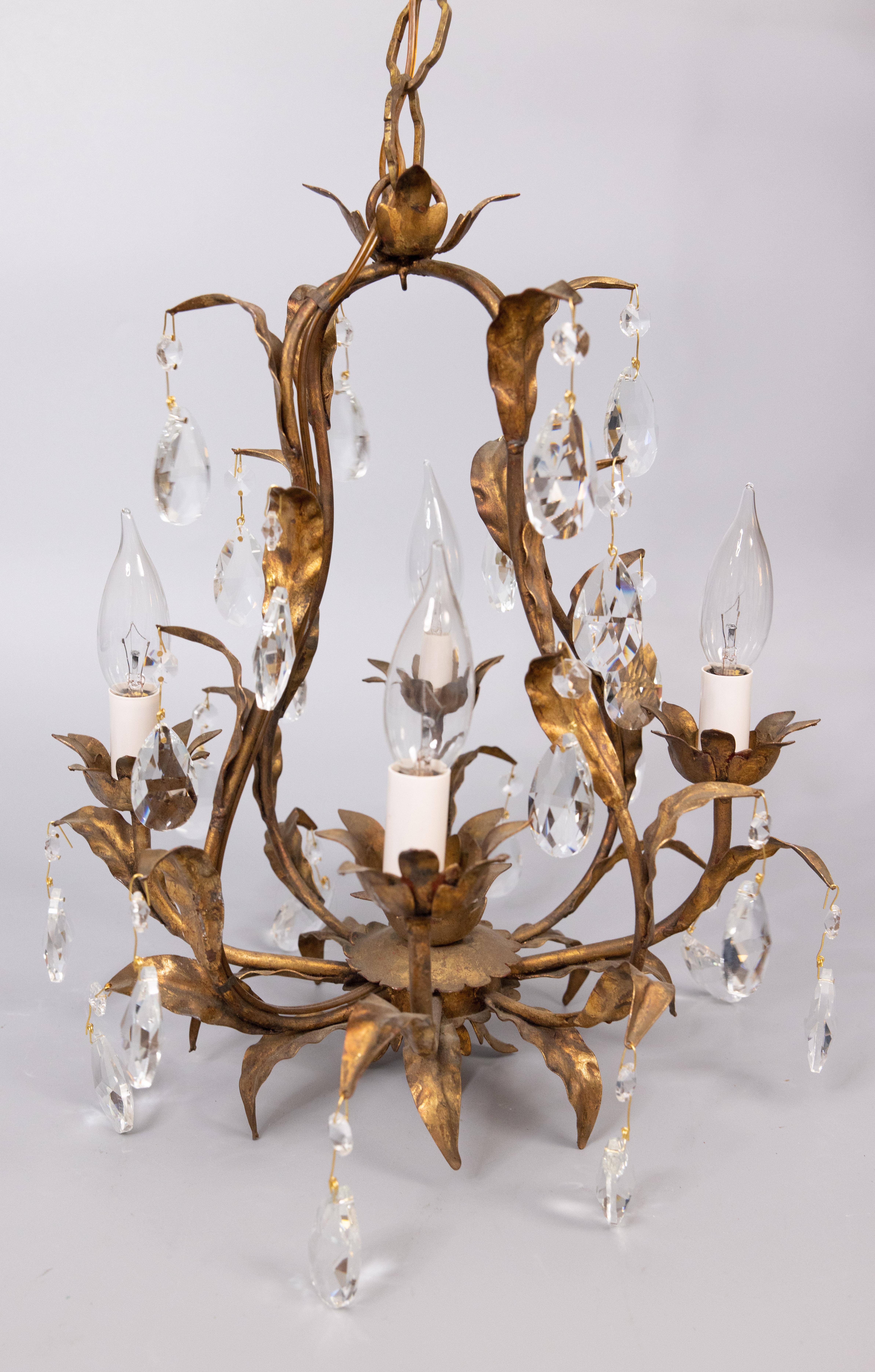 A stunning mid-20th century Italian gilded tole and crystals four arm chandelier. This gorgeous chandelier has crystals and scrolling leaves in a beautiful gilt patina and drippy wax candle sleeves. It's in excellent working condition and comes with