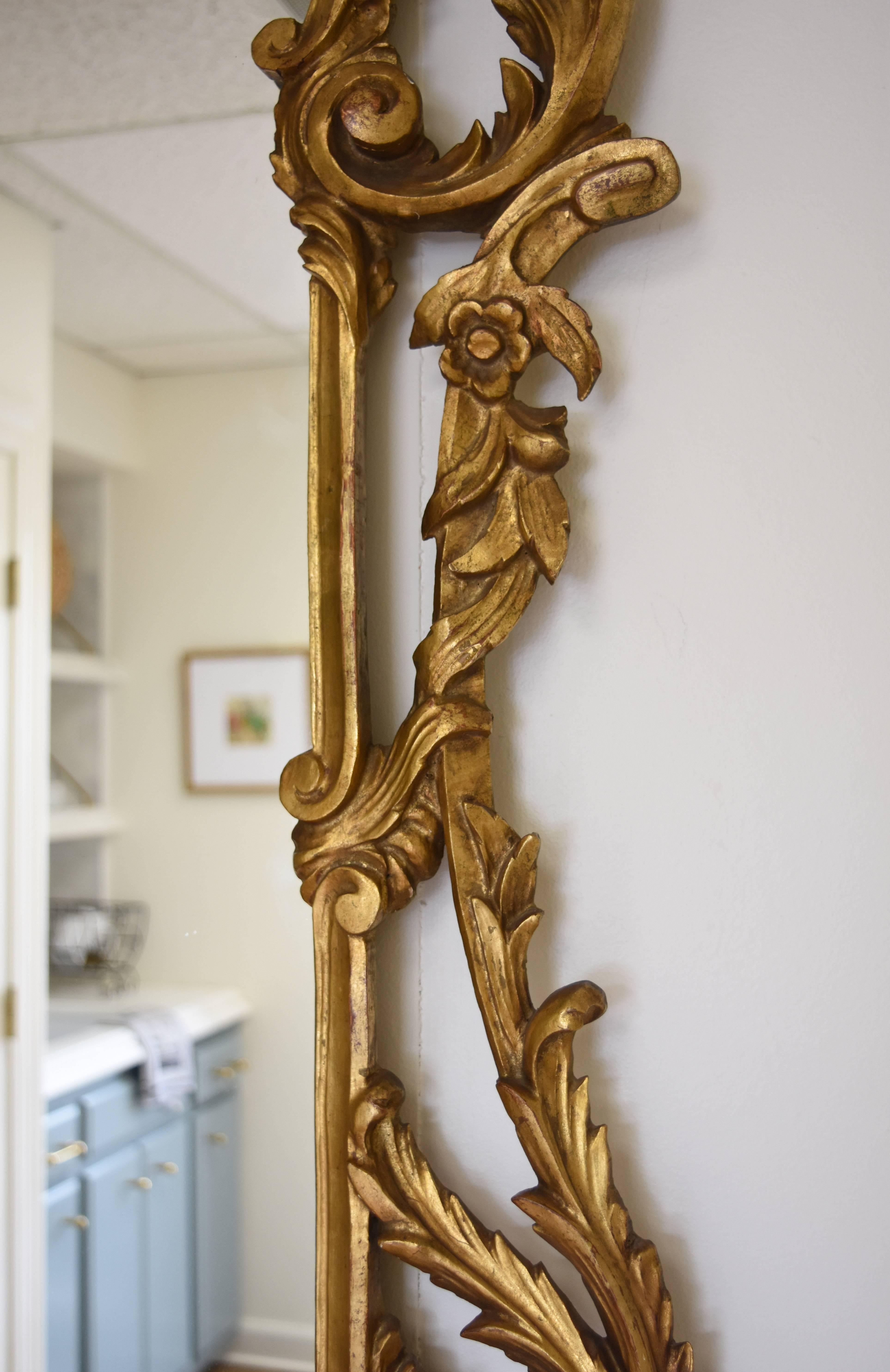 This vintage Italian giltwood mirror features carved scrolls and flowers. It is in the Rococo style and has a lovely gold finish.