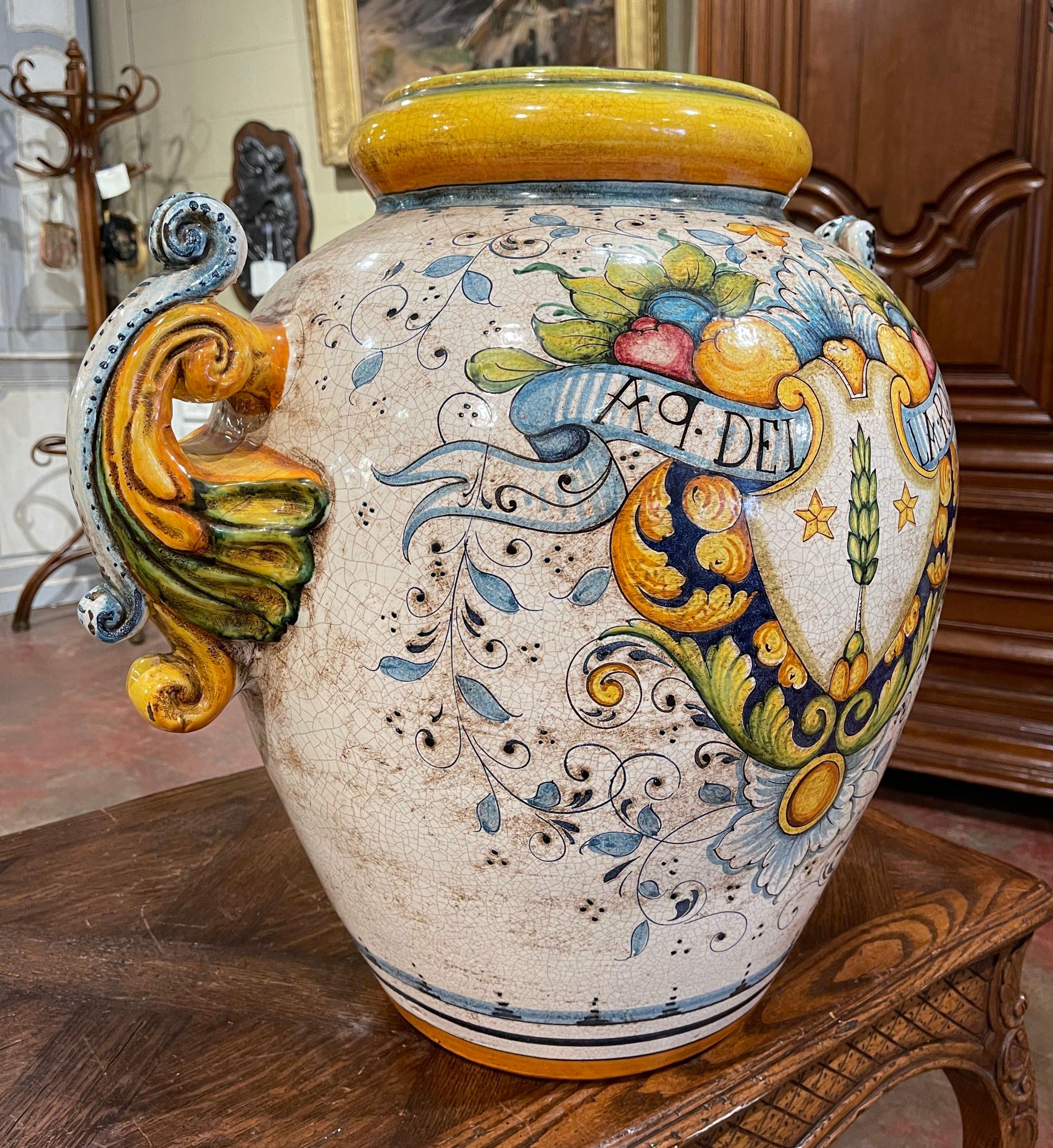Created in Italy circa 1960 and round in shape, the antique planter is decorated with elegant acanthus leaf side handles. The large ceramic cache pot features a yellow neck, and is decorated with a hand painted center medallion embellished with