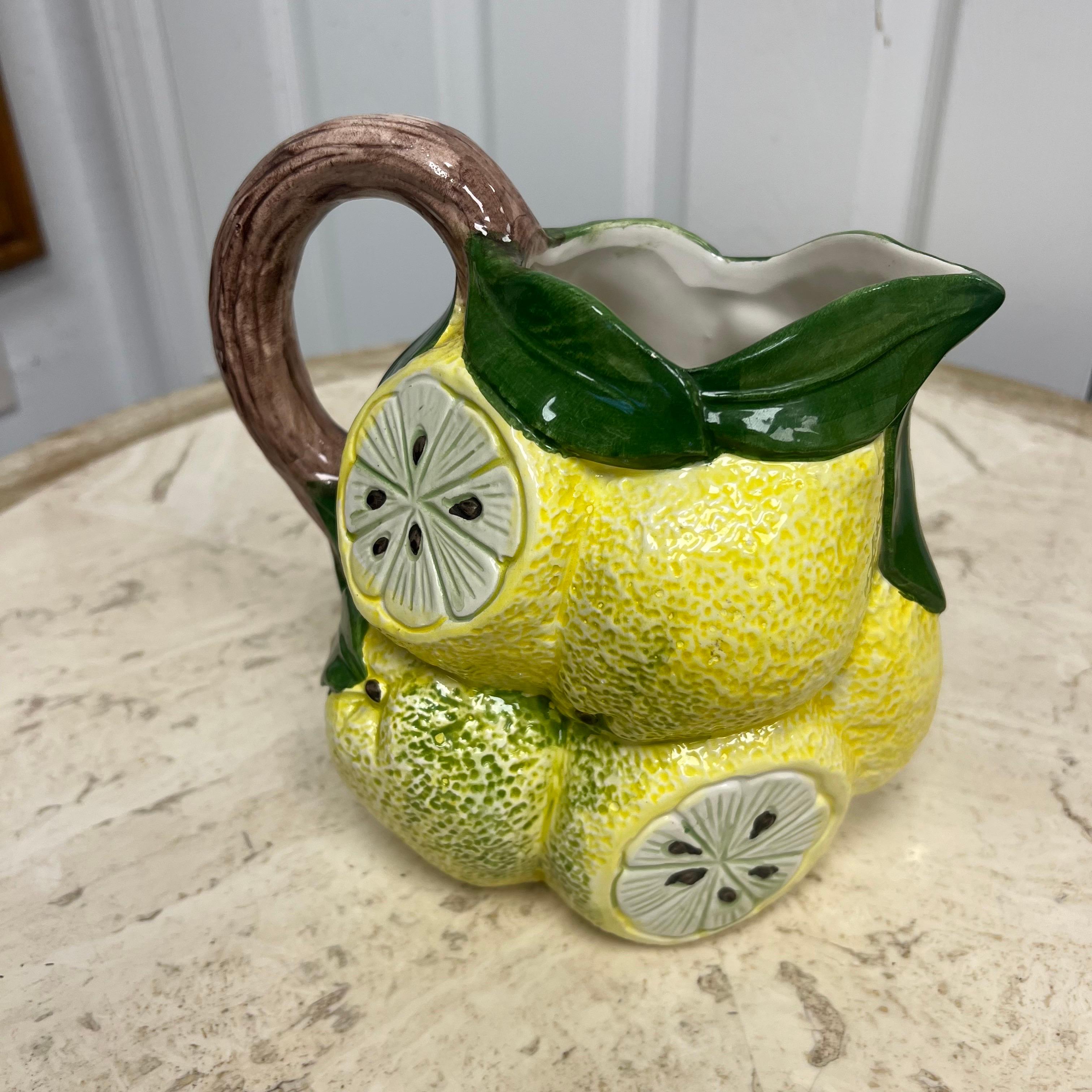 A vibrant hand-painted ceramic pitcher marked Made in Italy, crafted in the form of clustered lemons with leafy green accents and a sculptural branch handle. The body is richly detailed with textured surfaces and sliced lemon motifs, showcasing the