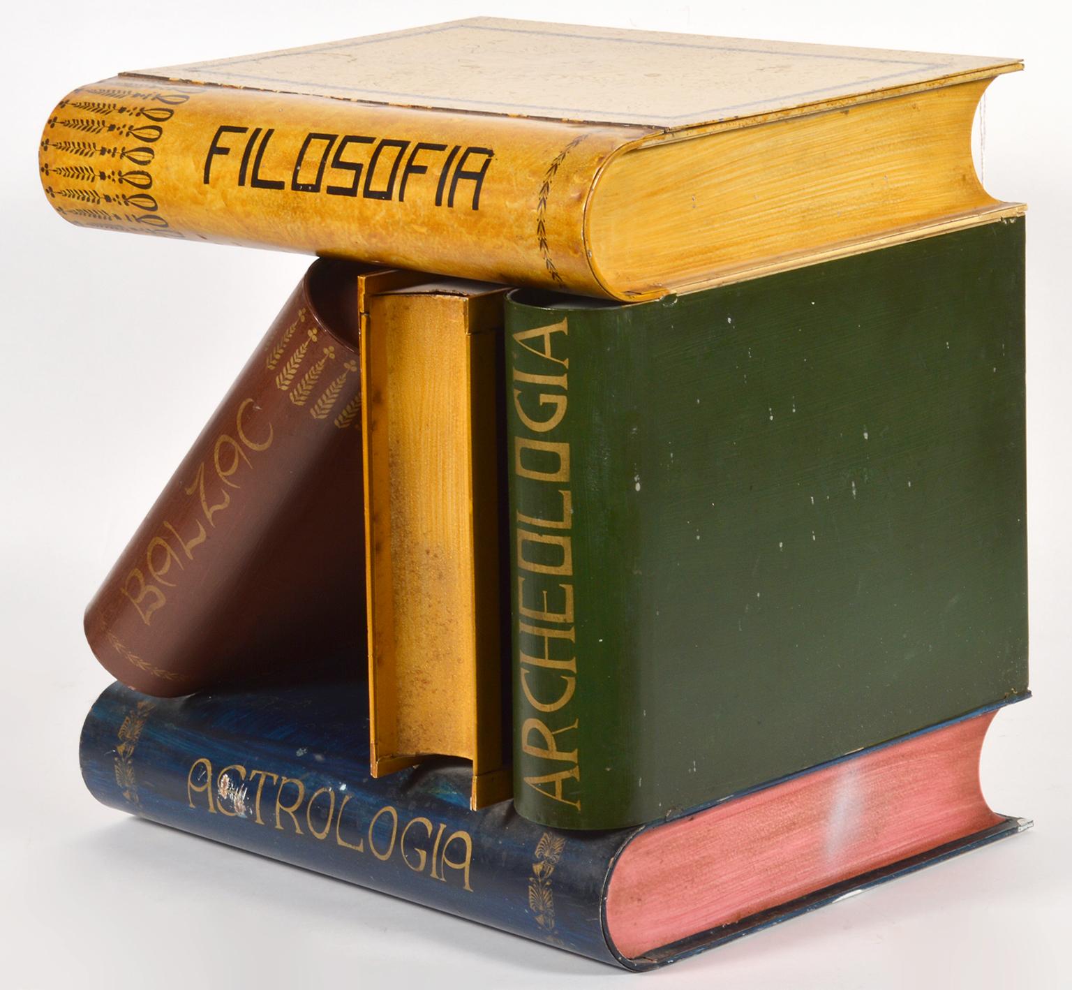 This sculptural table features 5 large faux books with titles in a composition involving one leaning book. It is made of steel tole and painted on all four sidess and the top opens up to a small storage box.