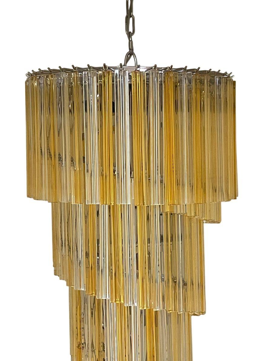 Un elegante lampadario a spirale italiano composto da prismi di vetro Venini trasparenti e ambrati alternati, sospesi a cascata a formare una scenografica silhouette a spirale. Gli elementi in vetro catturano e rifrangono la luce in modo