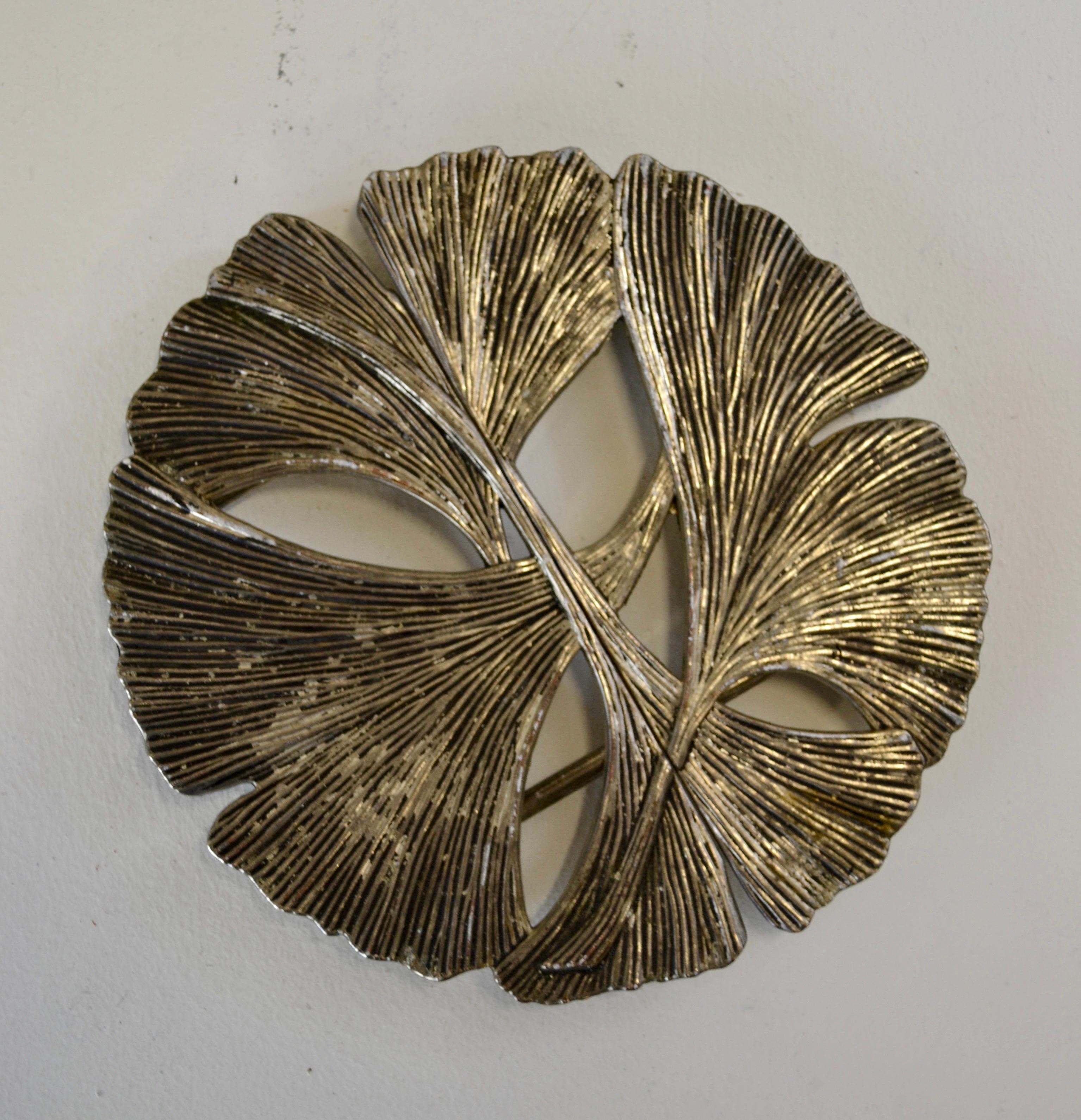 Dessous de plat télescopique italien raffiné du milieu du XXe siècle, fabriqué en métal et orné d'un motif de feuilles de ginkgo stylisées. Souvent confondu avec le bambou en raison de sa structure segmentée, le design s'inspire en réalité des