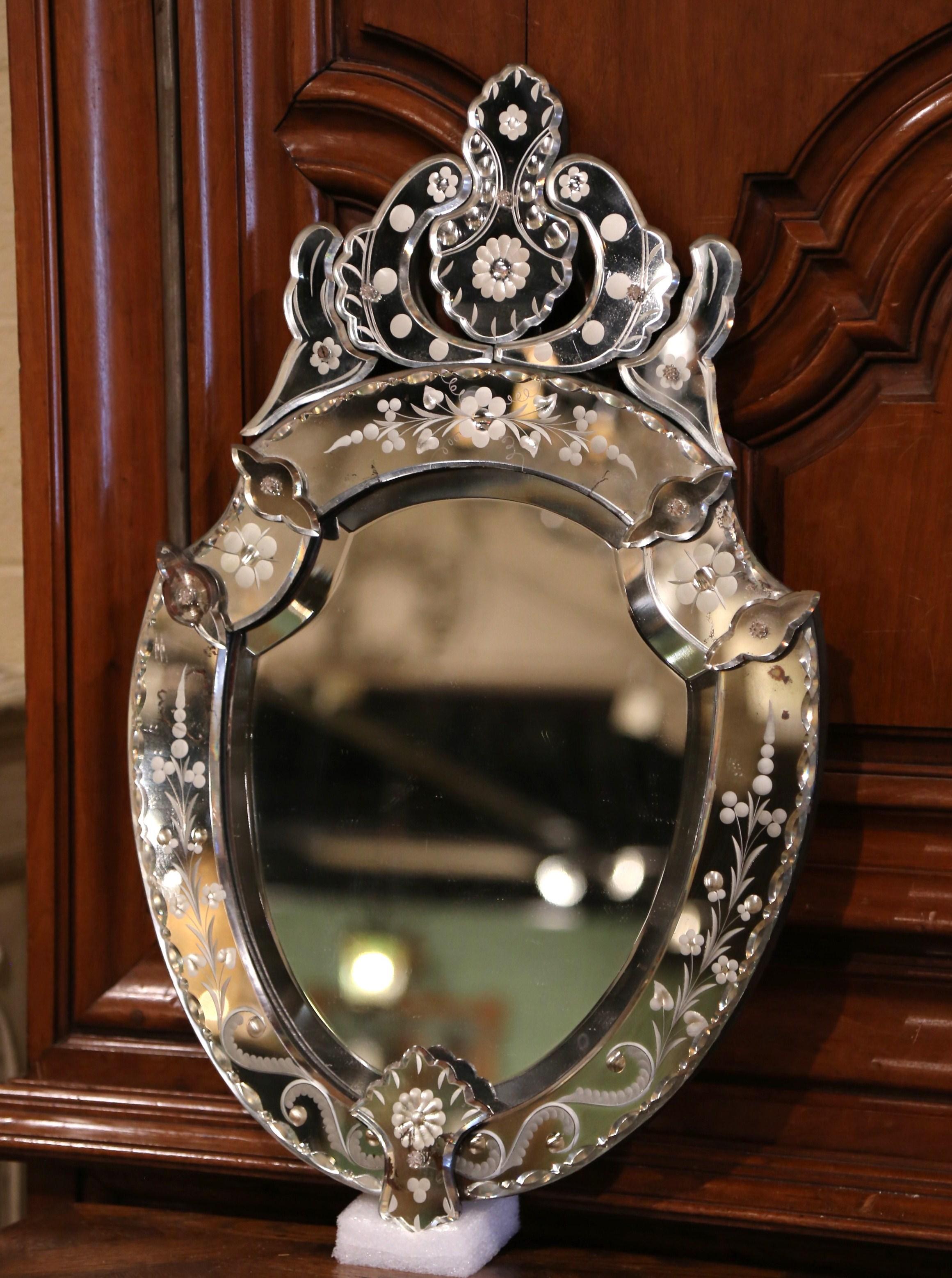 Decorate a powder room or a bedroom with this elegant, antique Venetian mirror. Crafted in Italy, circa 1960 and shaped as a shield, the wall mirror with carved decor at the pediment features hand painted floral etching between raised medallions