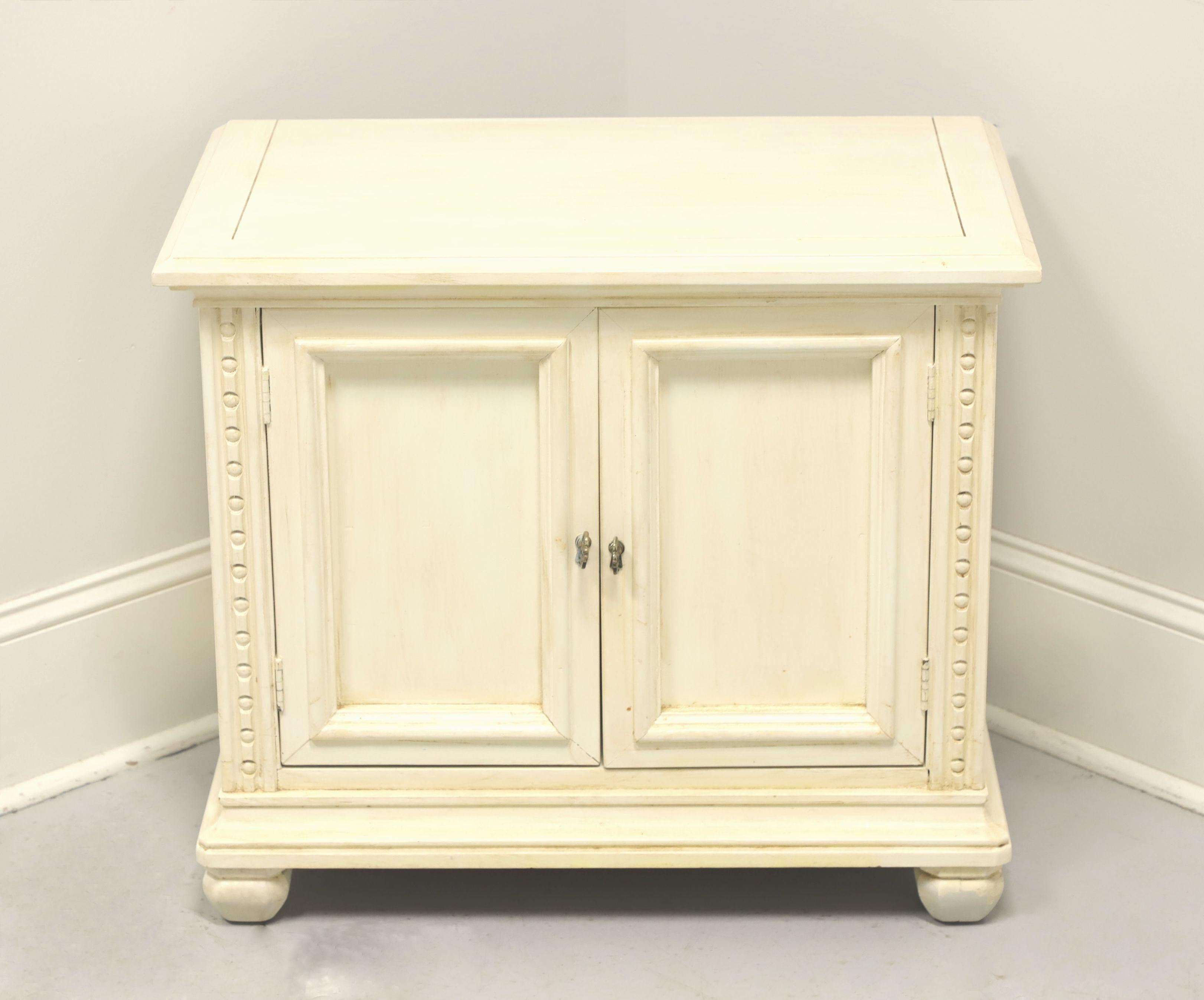 A Spanish style nightstand, unbranded, similar quality to Drexel or Henredon. Solid hardwood painted ivory, slightly distressed, brass hardware, banded top, carved front corners and turnip feet. Features two doors revealing one drawer of dovetail