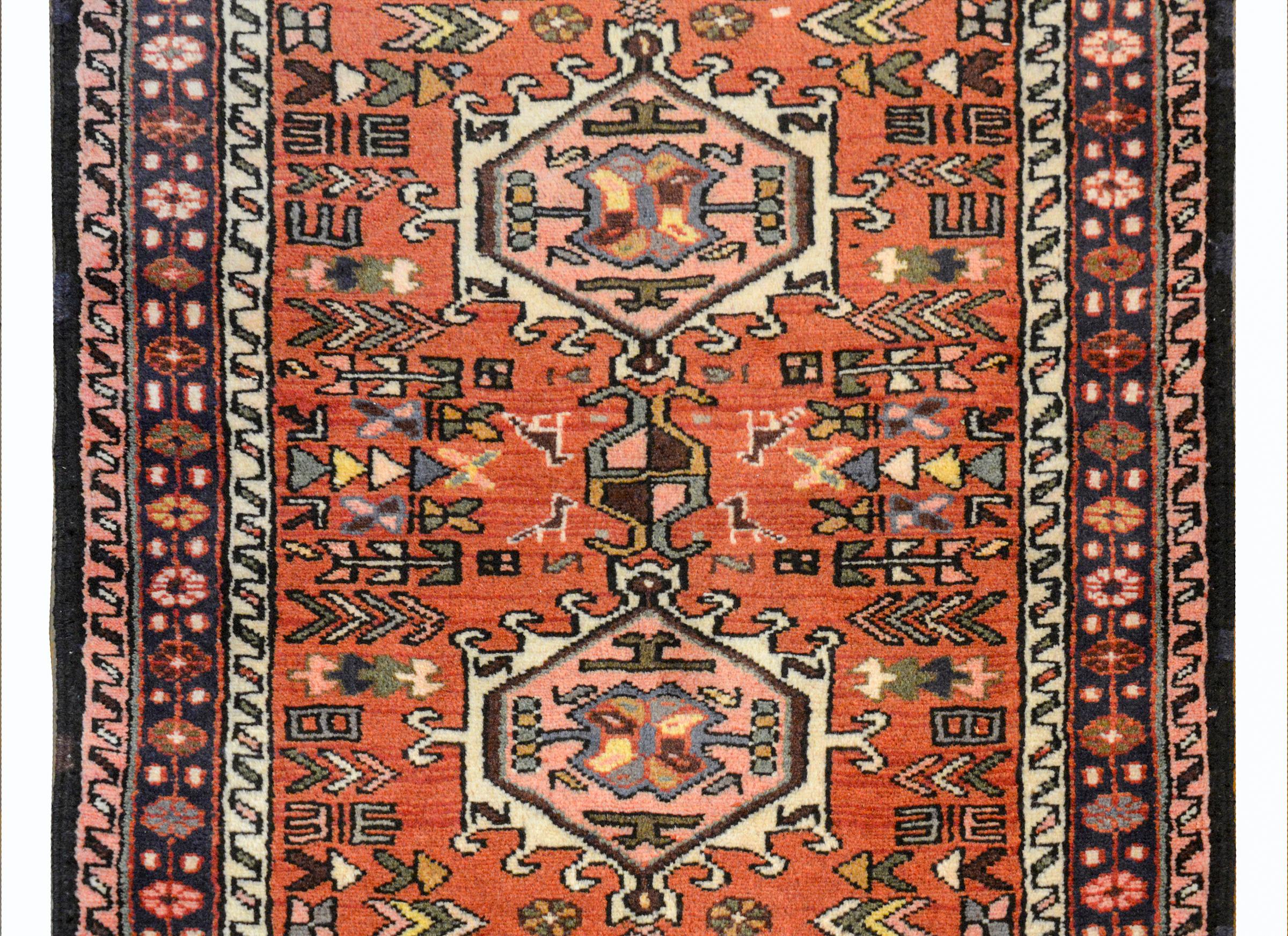 A wonderful mid-20th century Persian Karadja runner with several stylized floral medallions woven in myriad colors including violet, pink, white, coral, gray, and gold amidst a field of more stylized flowers against a coral background. The border is