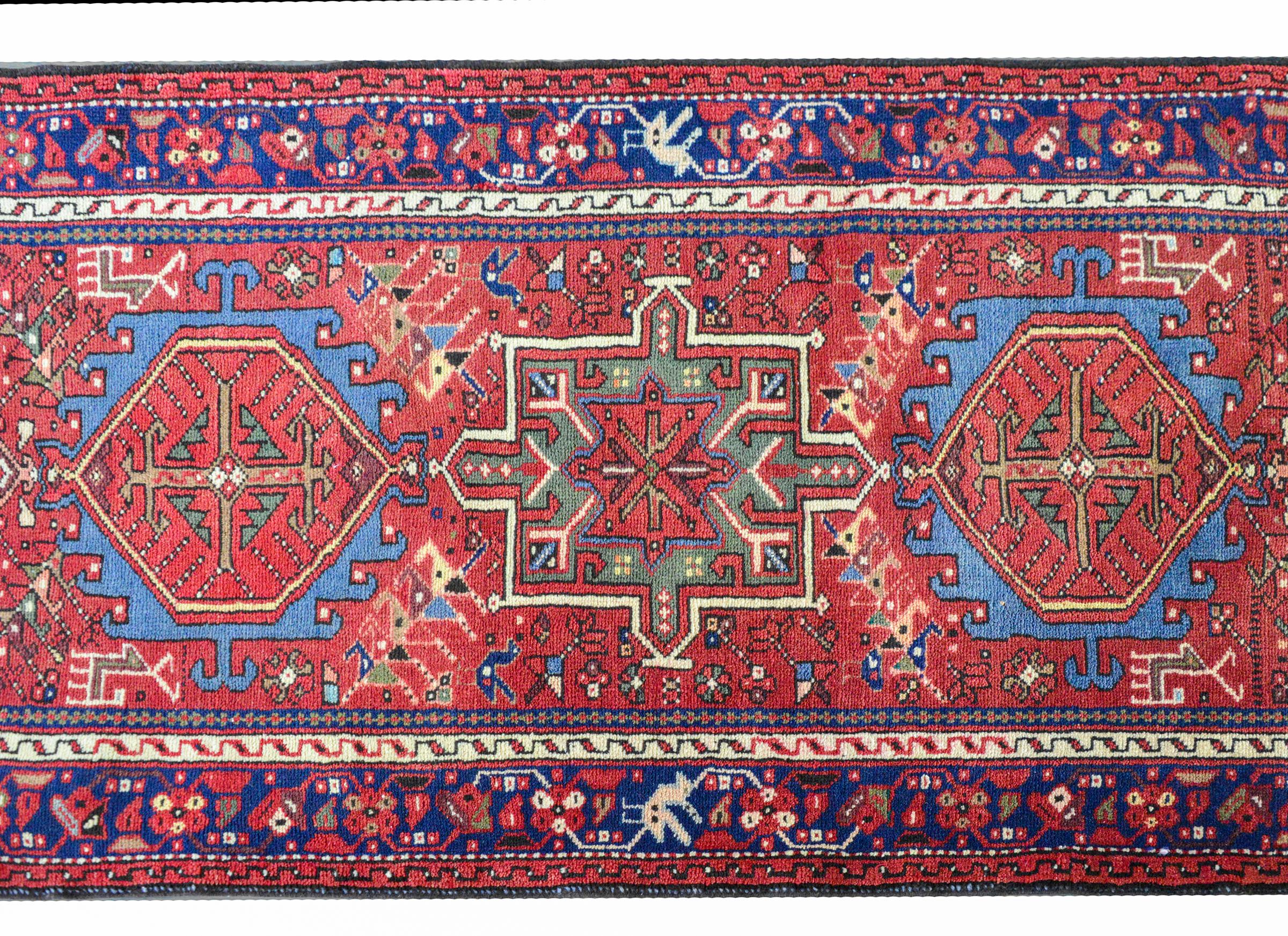 A wonderful mid-20th century Persian Karadja runner with several stylized floral medallions woven in myriad colors including indigo, pink, white, crimson, and green, amidst a field of more stylized flowers against a crimson background. The border is