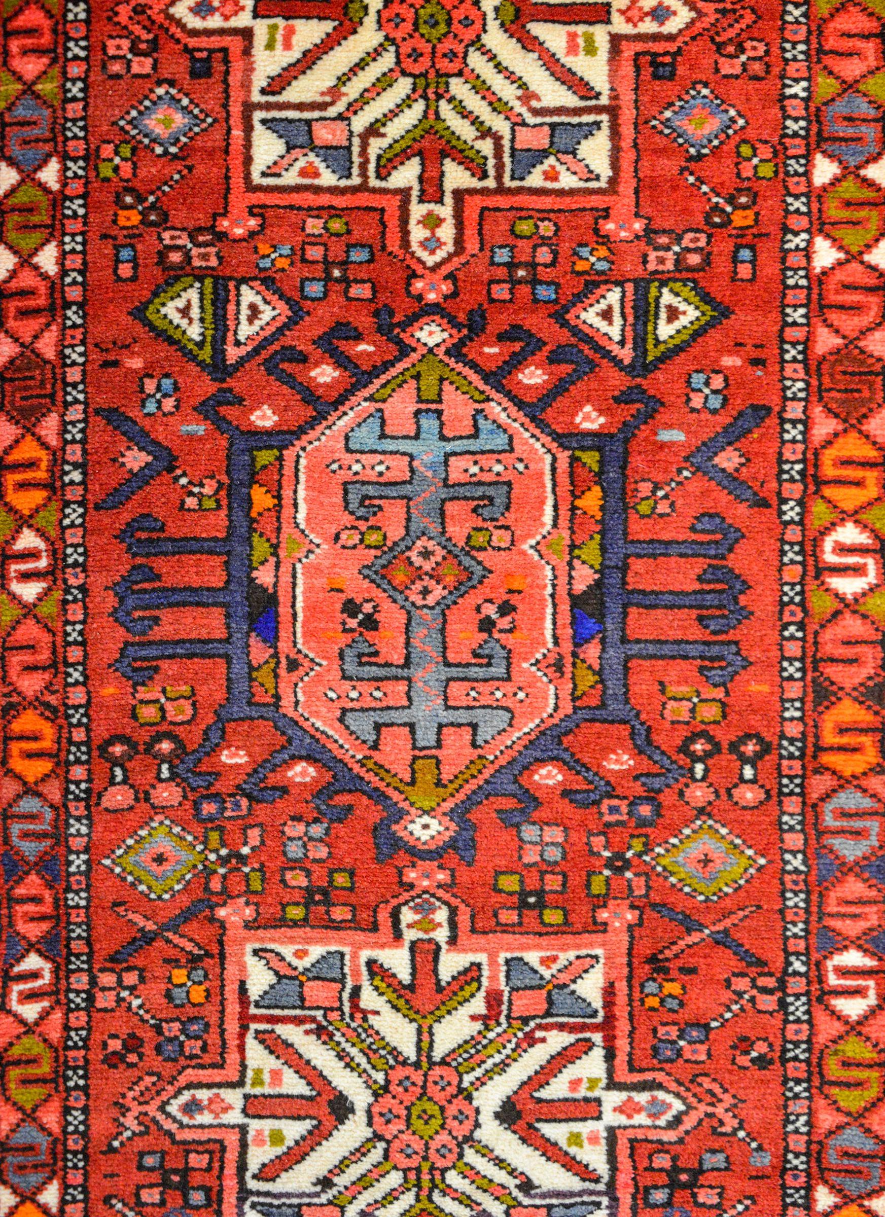 A wonderful mid-20th century Persian Karadja runner with several stylized floral medallions woven in myriad colors including indigo, pink, white, crimson, green, and gold amidst a field of more stylized flowers against a crimson background. The