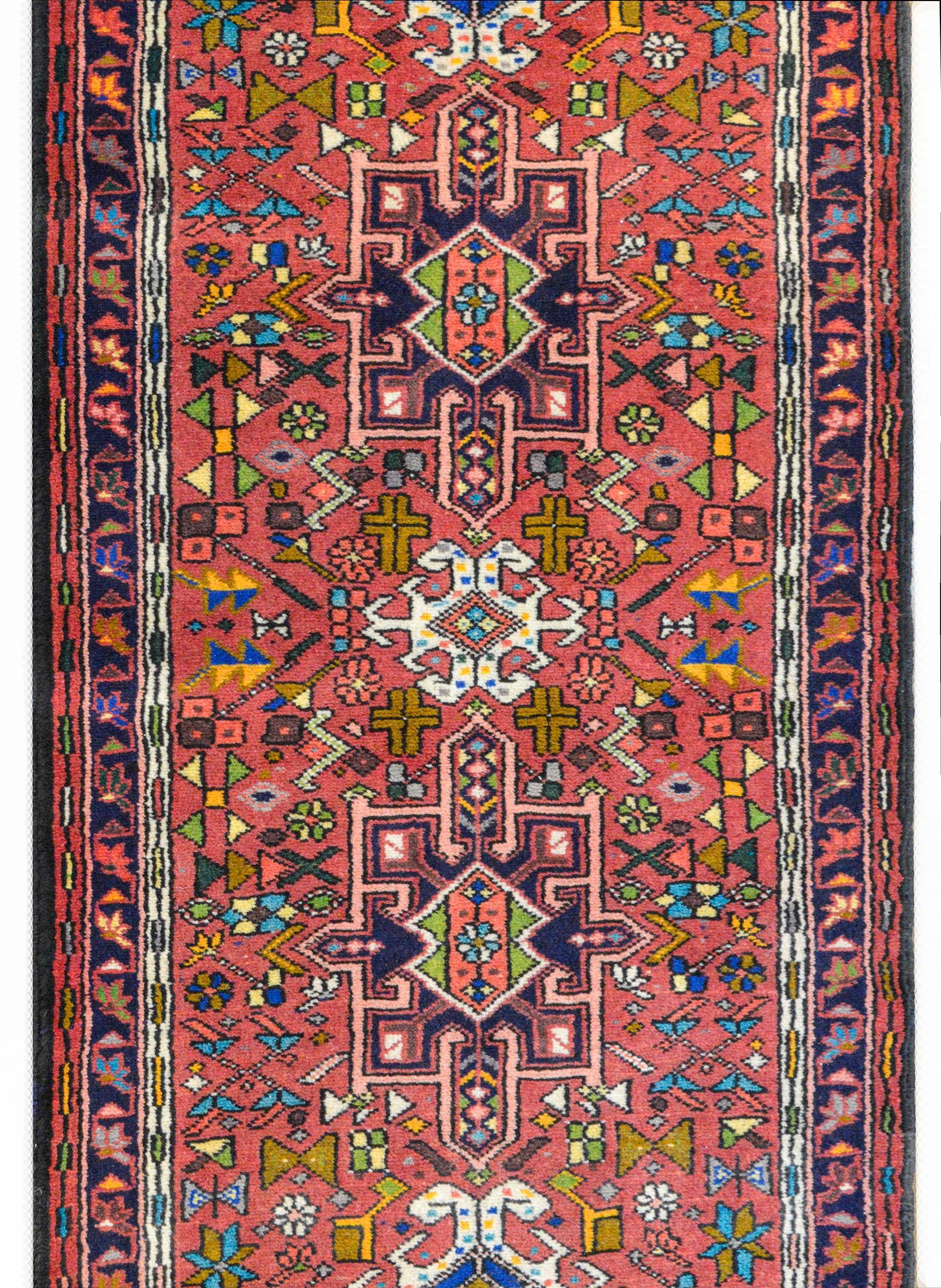 A wonderful mid-20th century Persian Karadja runner with several stylized floral medallions woven in black, pink, light blue, gold, green, and white amidst a field of more stylized flowers against a muted crimson background. The border is wonderful