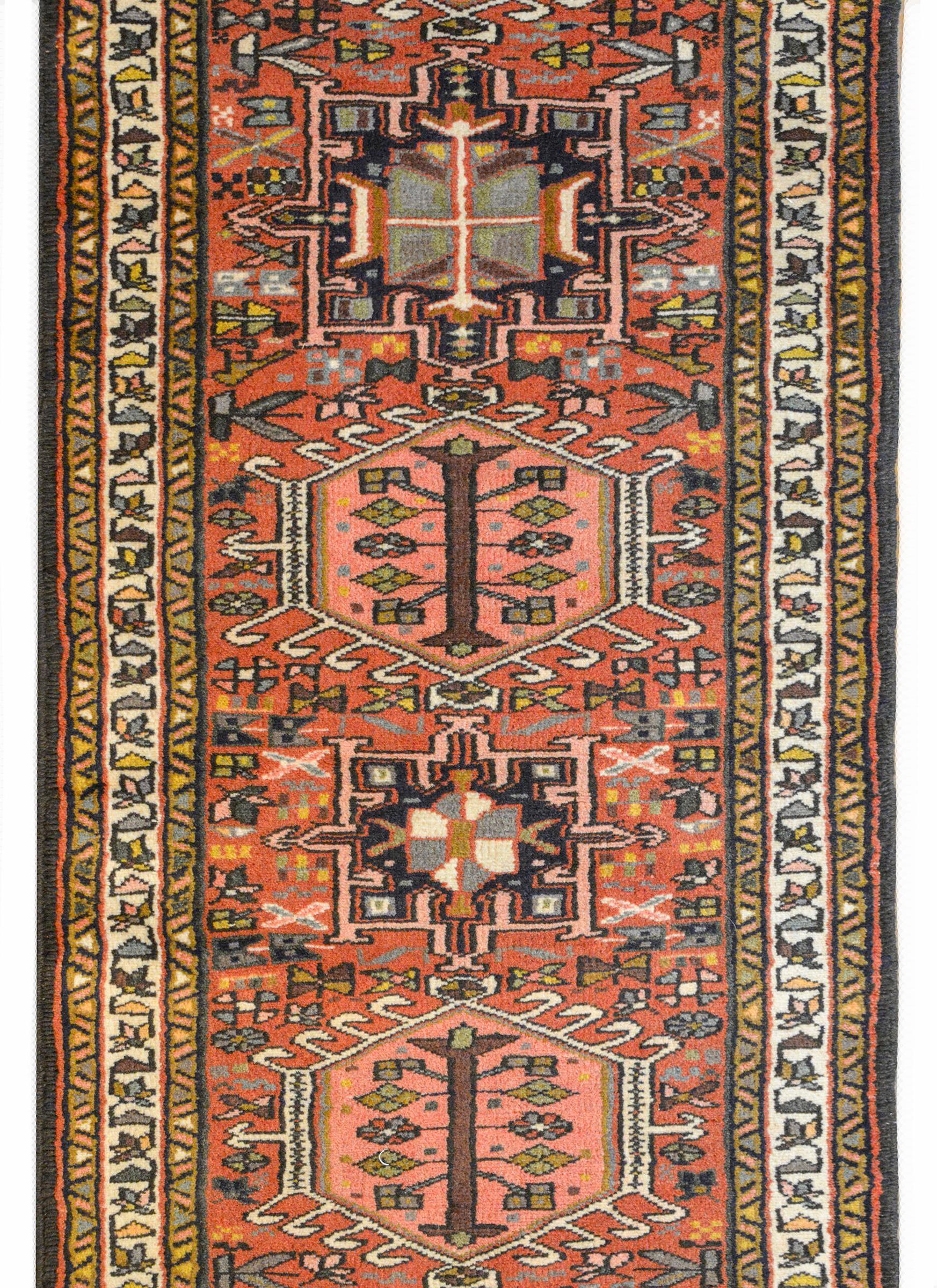 A wonderful mid-20th century Persian Karadja runner with several stylized floral medallions woven in black, pink, light blue, gold and white amidst a field of more stylized flowers against a pale crimson background. The border is wonderful composed