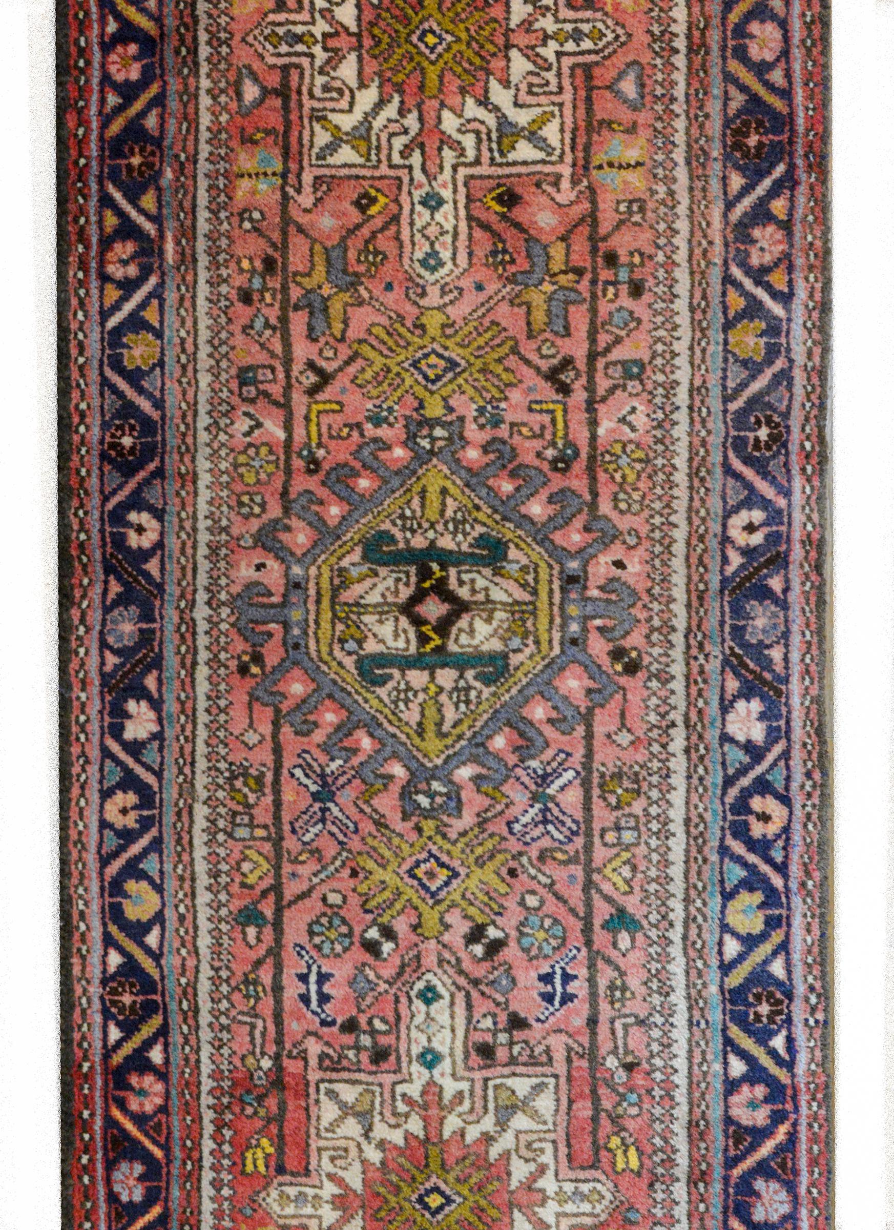 A wonderful mid-20th century Persian Karadja runner with multiple stylized floral medallions woven in indigo, pink, gold and green amidst a field of more stylized flowers and leaves against a pale cranberry background. The border is wonderful