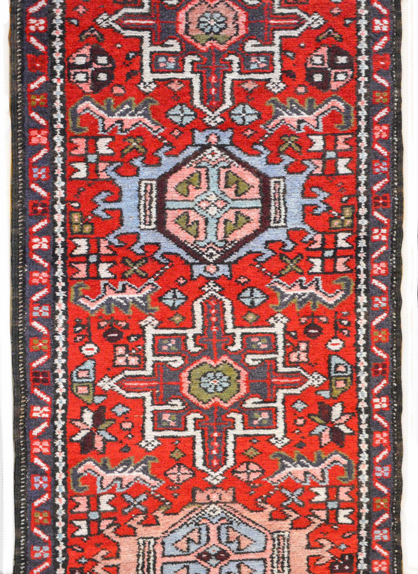 A wonderful mid-20th century Persian Karadja runner with several stylized floral medallions woven in myriad colors including indigo, pink, white, crimson, and green, amidst a field of more stylized flowers against a crimson background. The border is